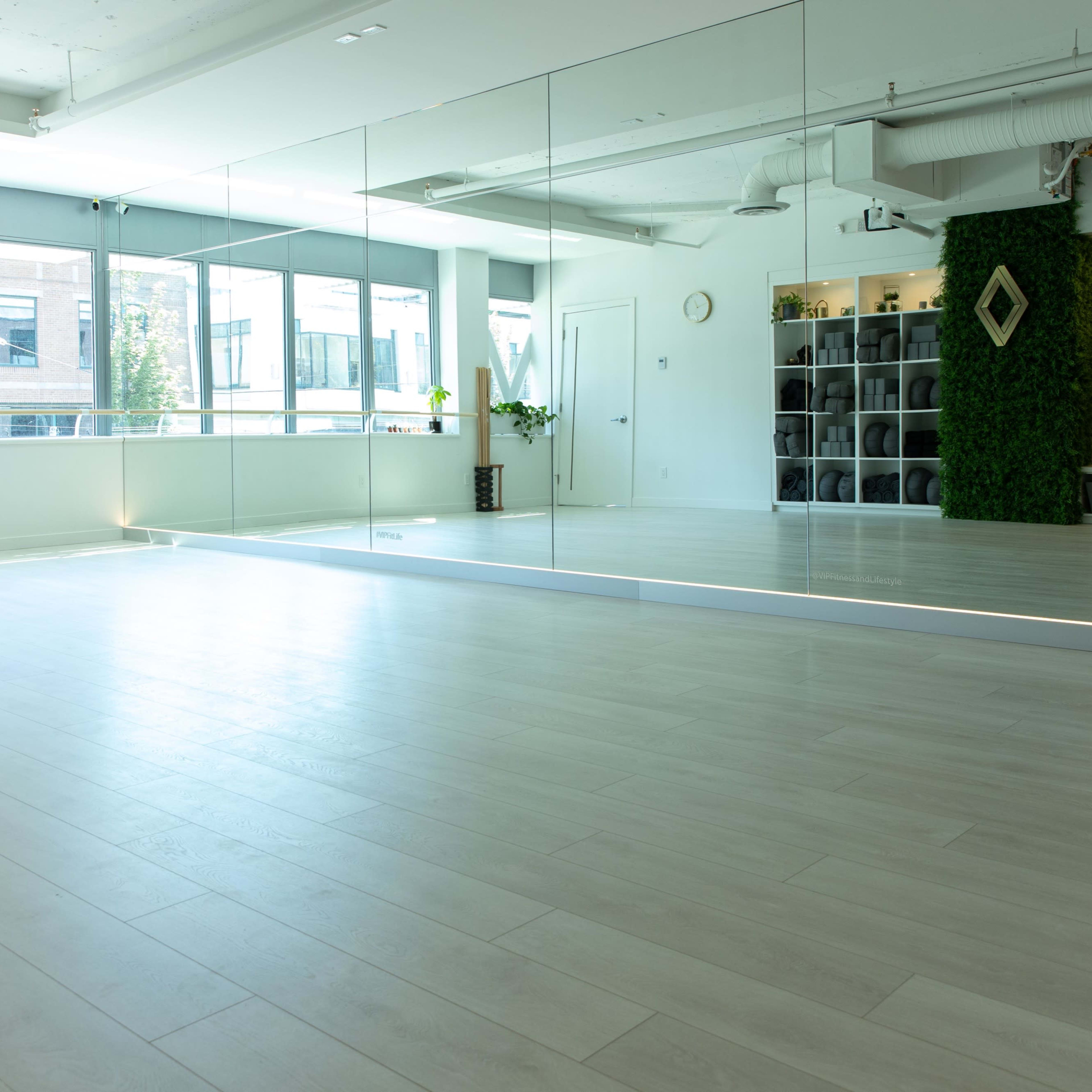 A spacious, well-lit studio with large mirrors, wooden flooring, and a green wall feature, complemented by shelves in the background.