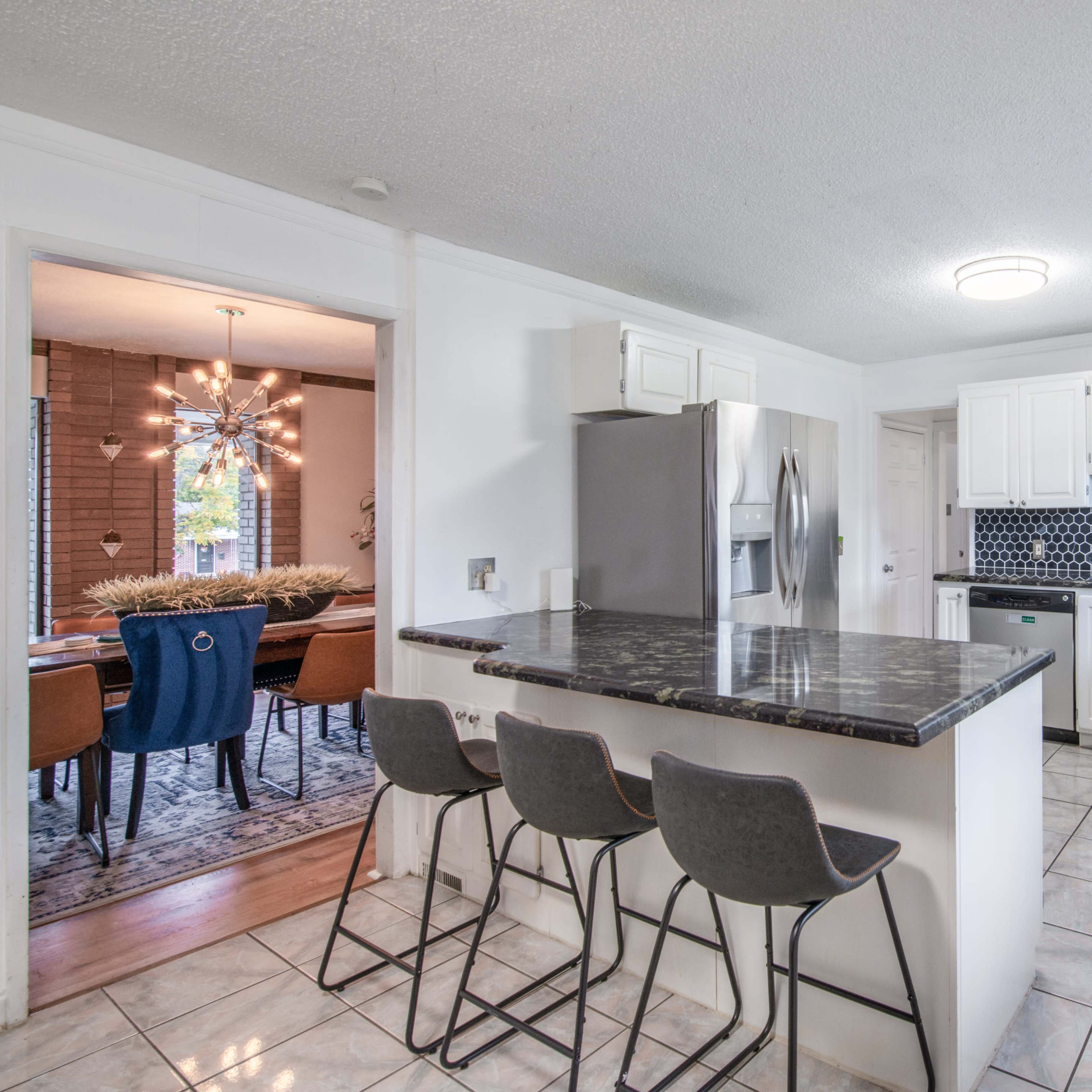 A modern kitchen with a granite island and four bar stools, featuring white cabinets and a black tile backsplash.