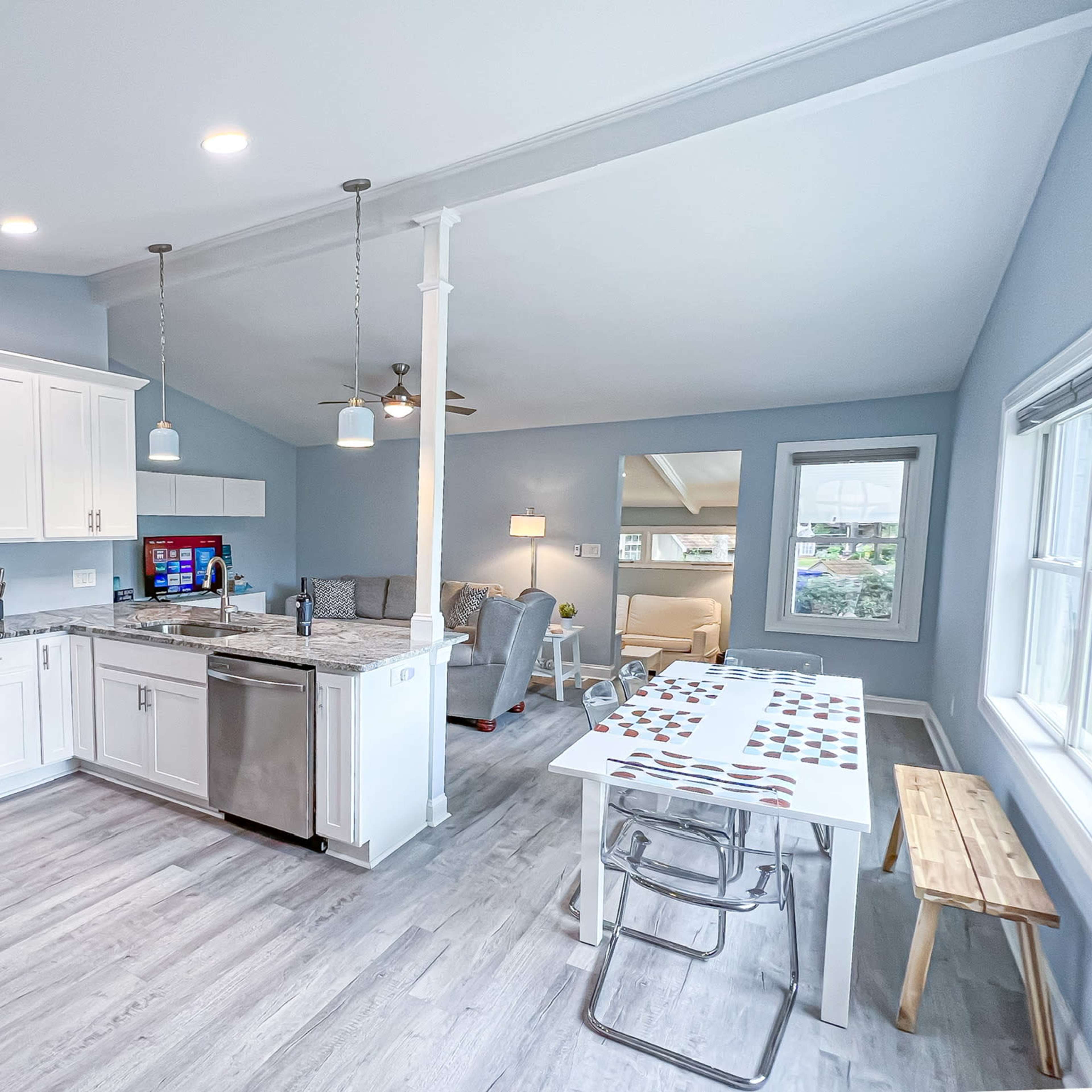 A modern kitchen with white cabinets, stainless steel appliances, and a dining table set for four, adjacent to a cozy living area.