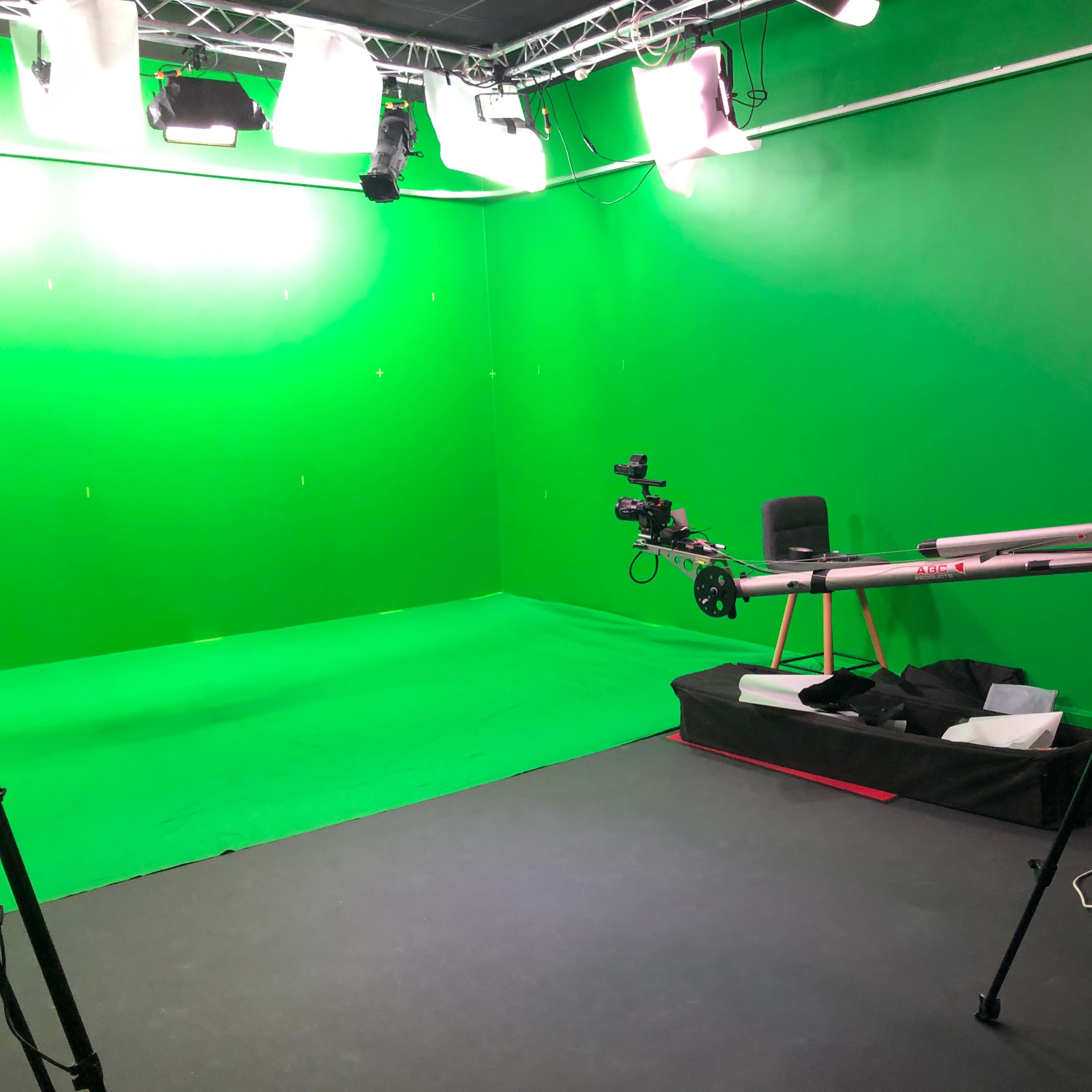 A green screen studio setup with a camera on a tripod, a camera dolly, and studio lighting equipment.