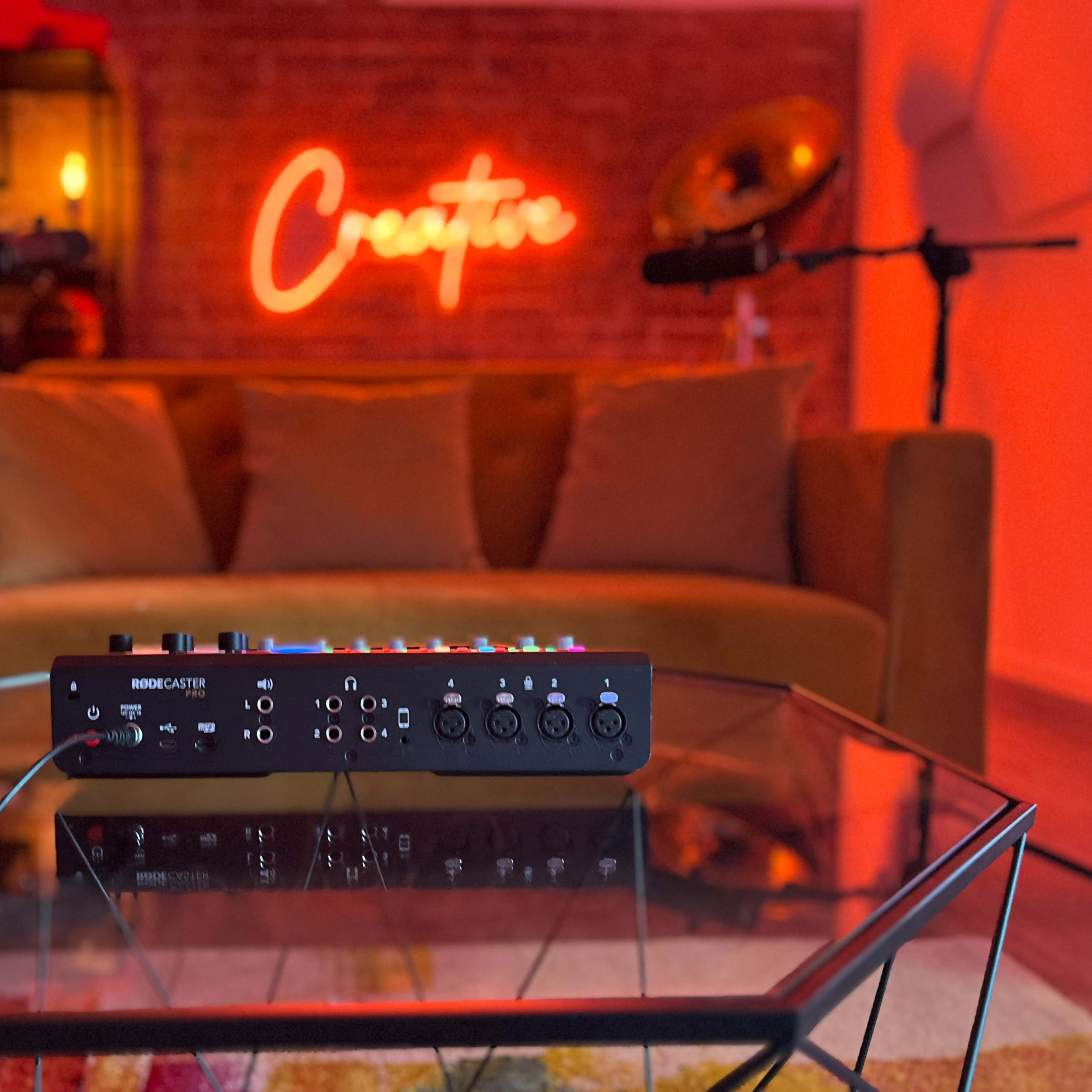 A music mixer placed on a glass table in a cozy room with a neon sign that reads "Creator" and a brown couch in the background.