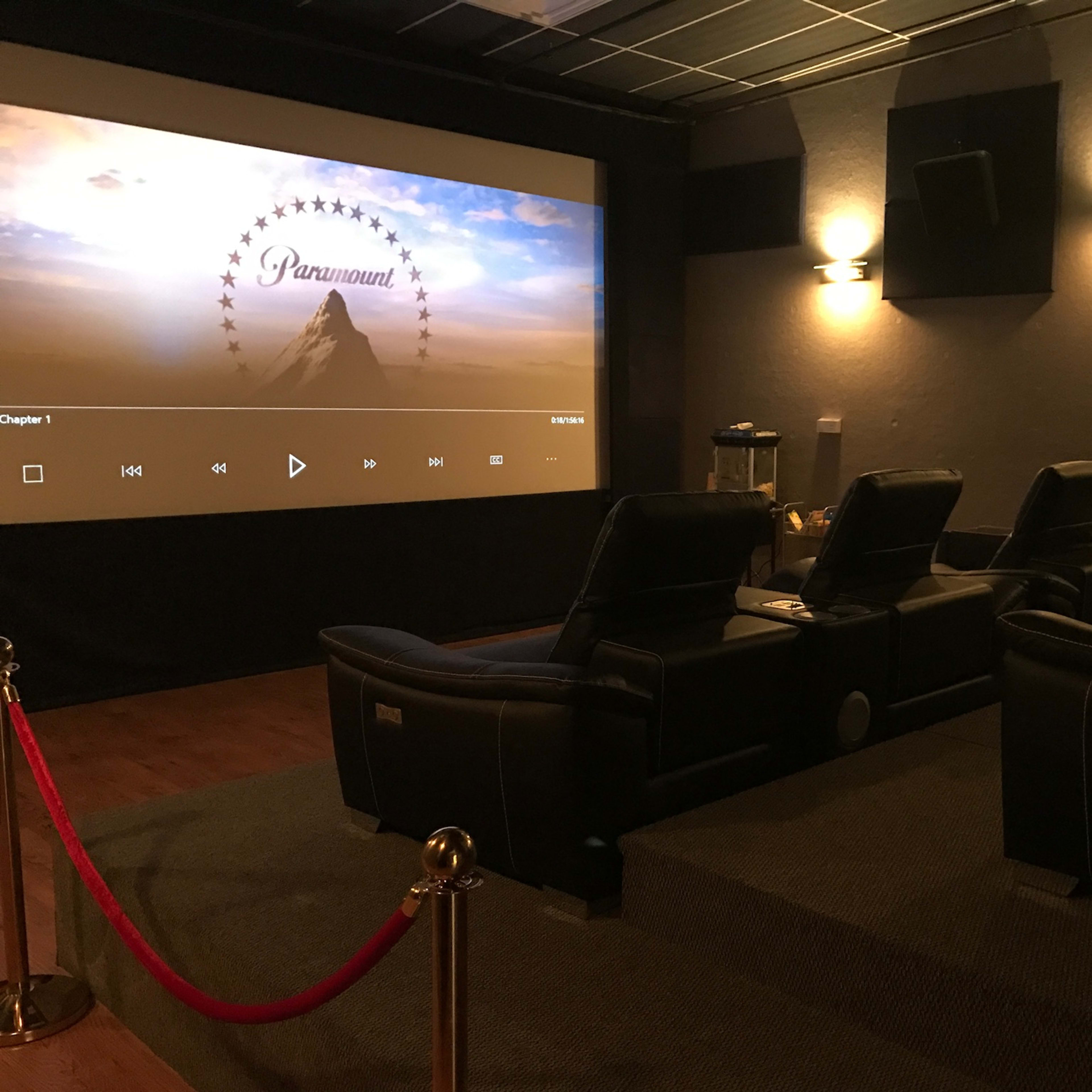 A private home theater with reclining seats arranged in front of a large screen displaying the Paramount logo.