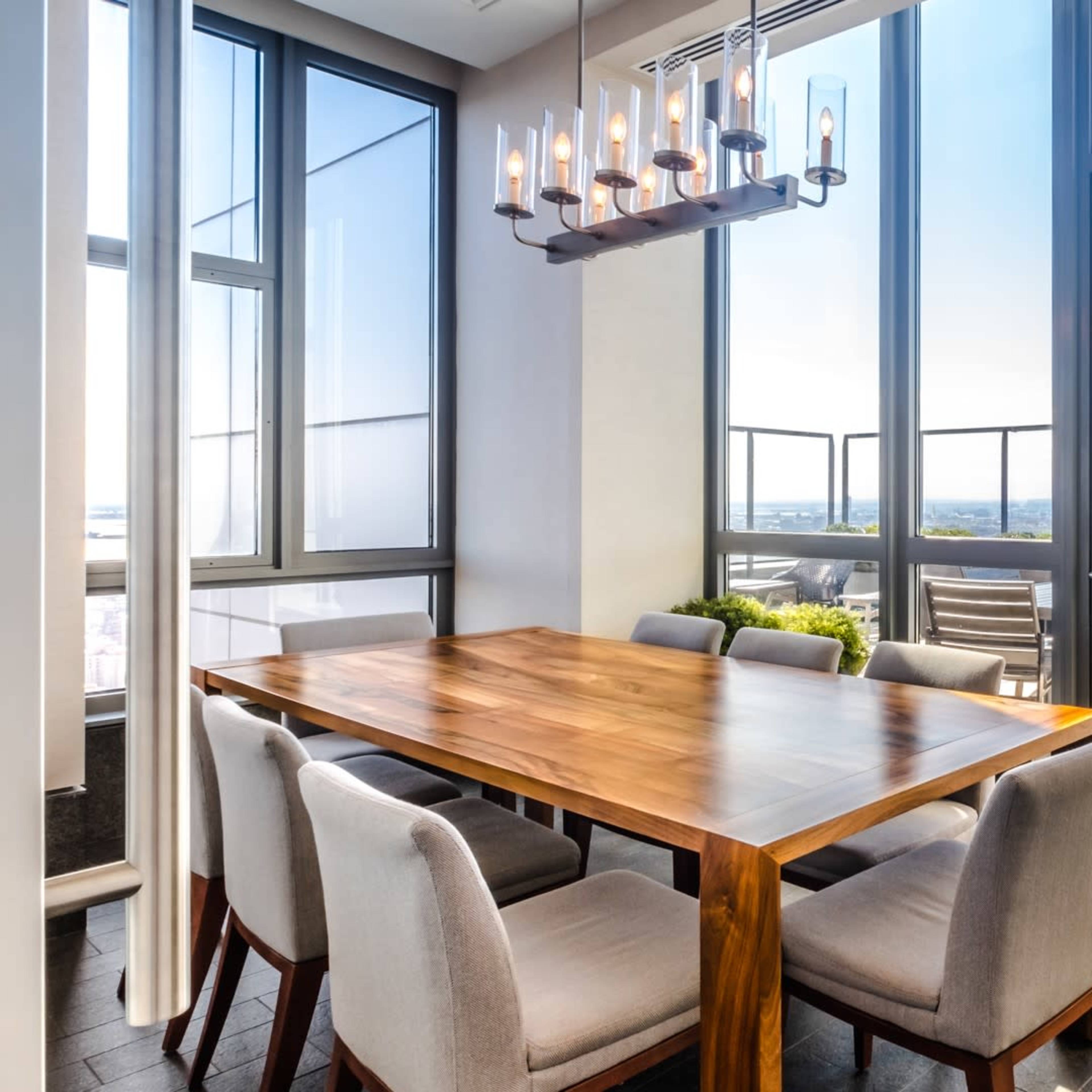 A dining area features a wooden table surrounded by upholstered chairs, with large windows offering a view of an outdoor terrace.