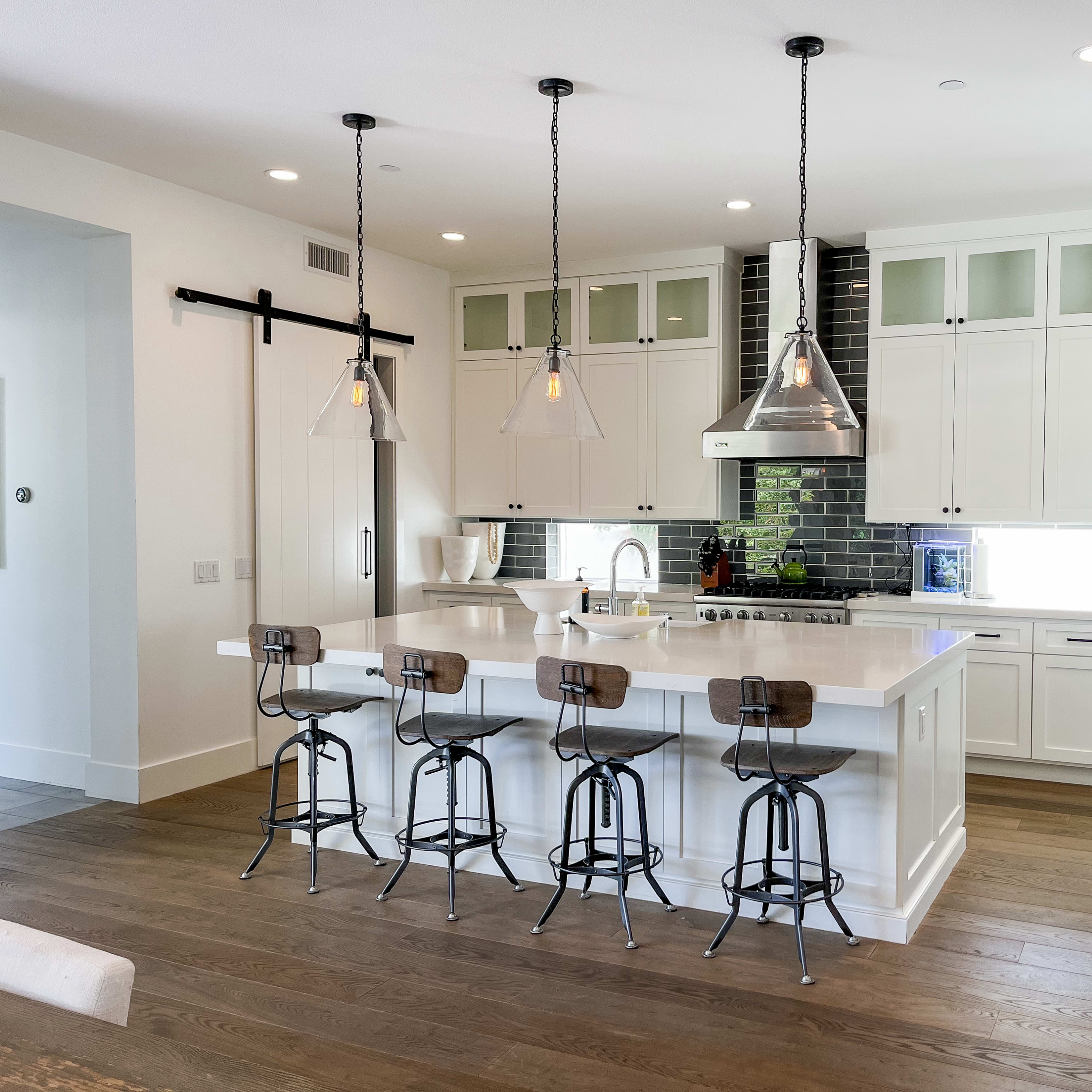 A modern kitchen with white cabinetry, a large island with bar stools, and pendant lighting above.