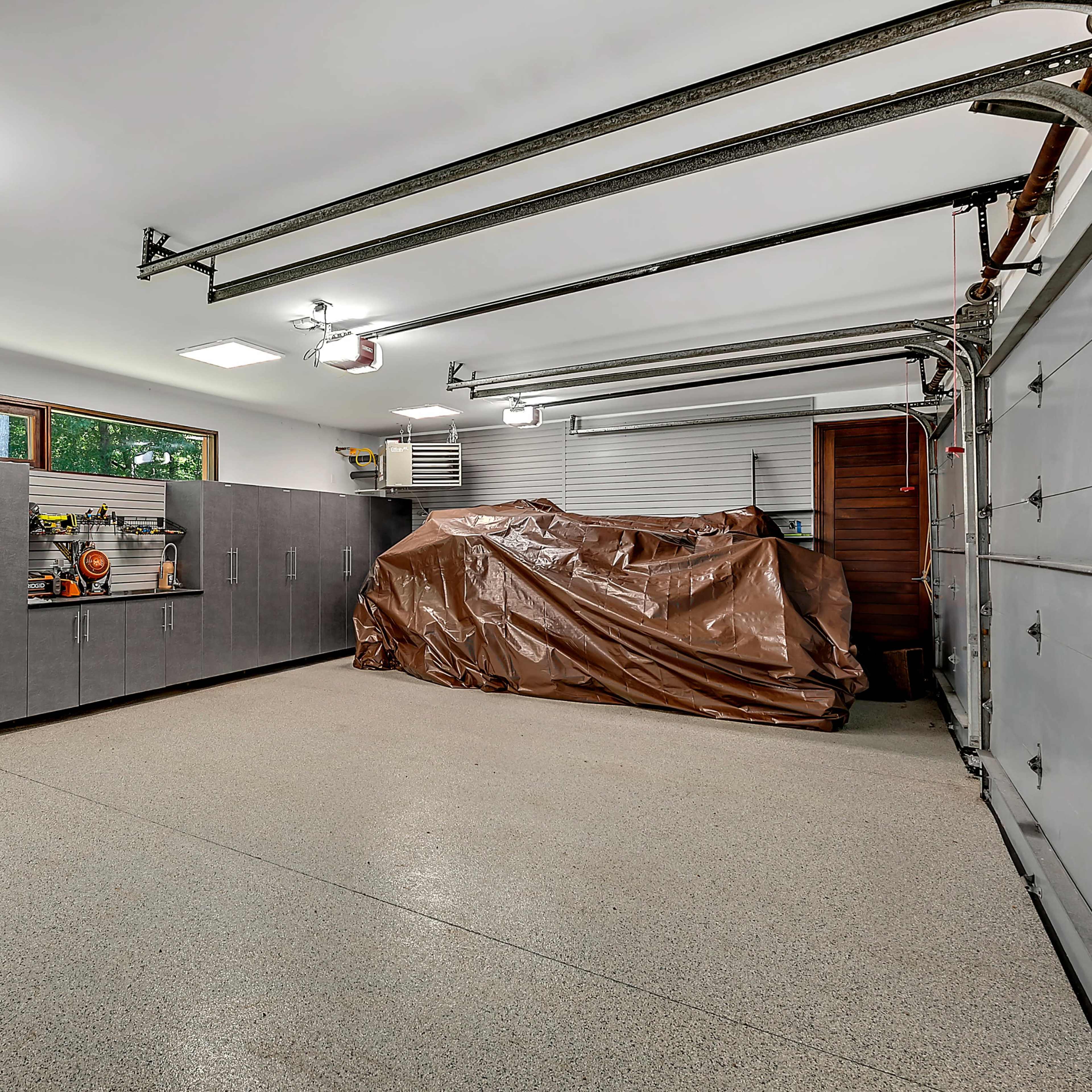 A clean garage with gray cabinets and a large brown tarp covering an object in the corner.
