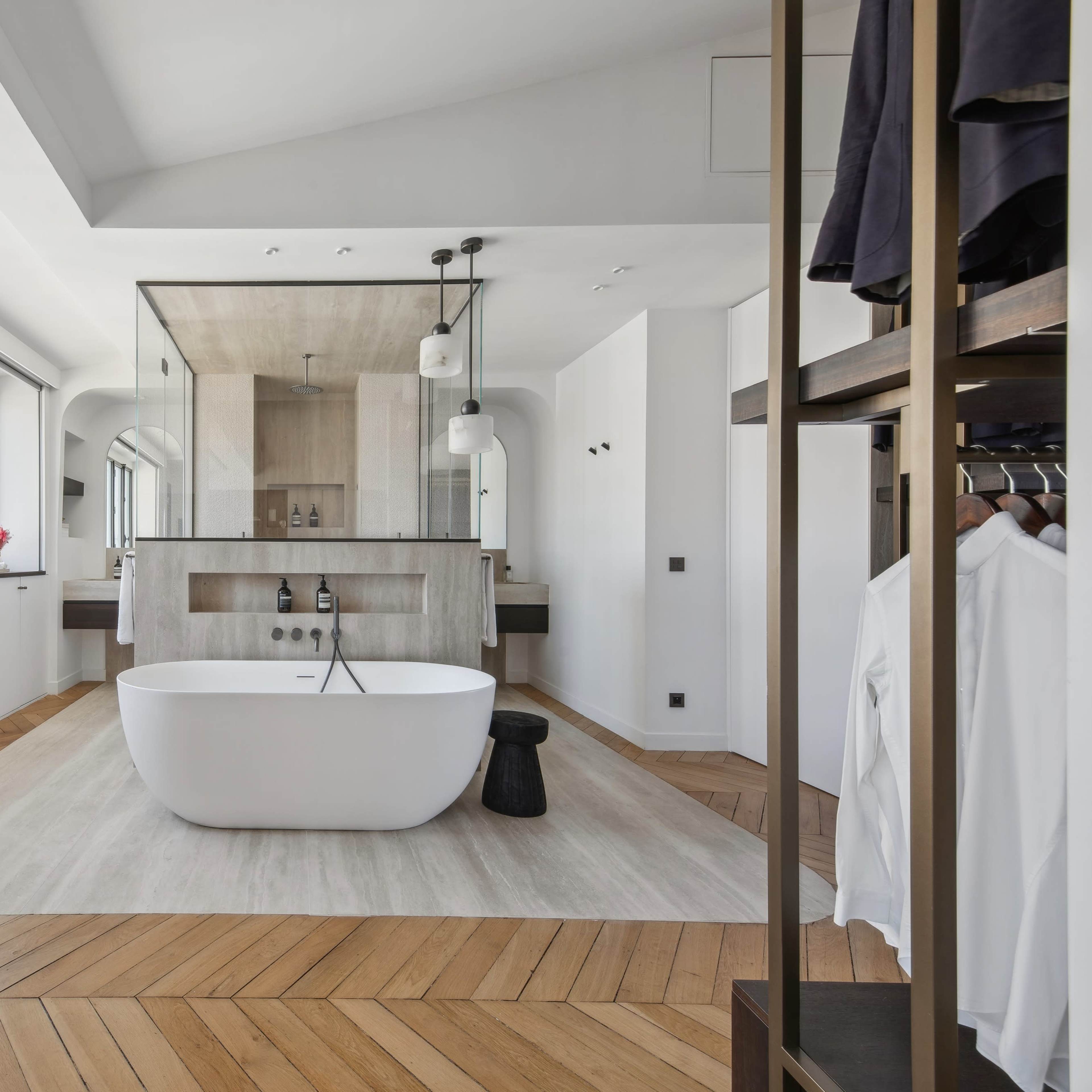 A modern bathroom featuring a freestanding white bathtub, a wooden floor, and large windows that allow natural light to enter the space.