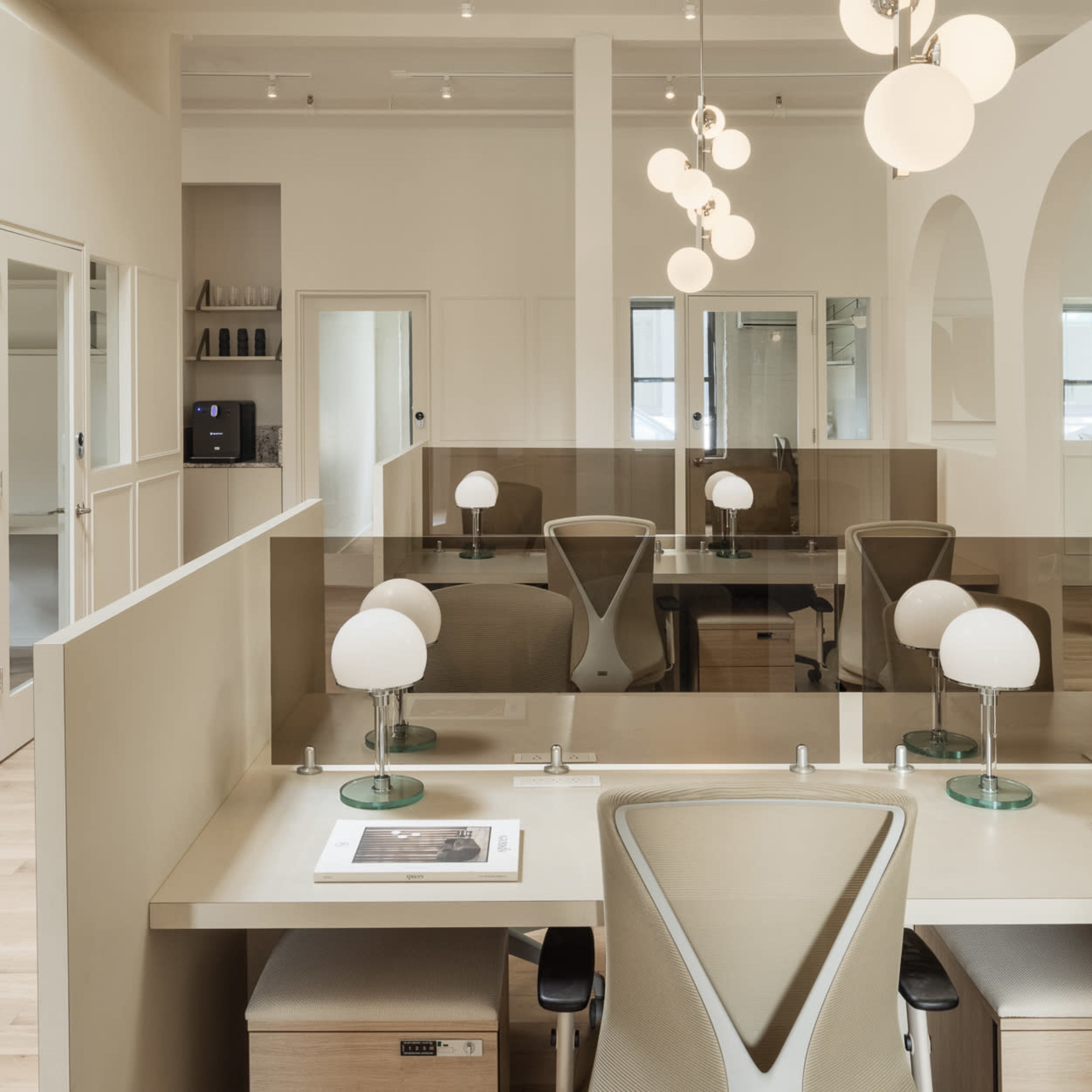 A modern office space with light-colored walls, arched doorways, and desks equipped with lamps and partitions.