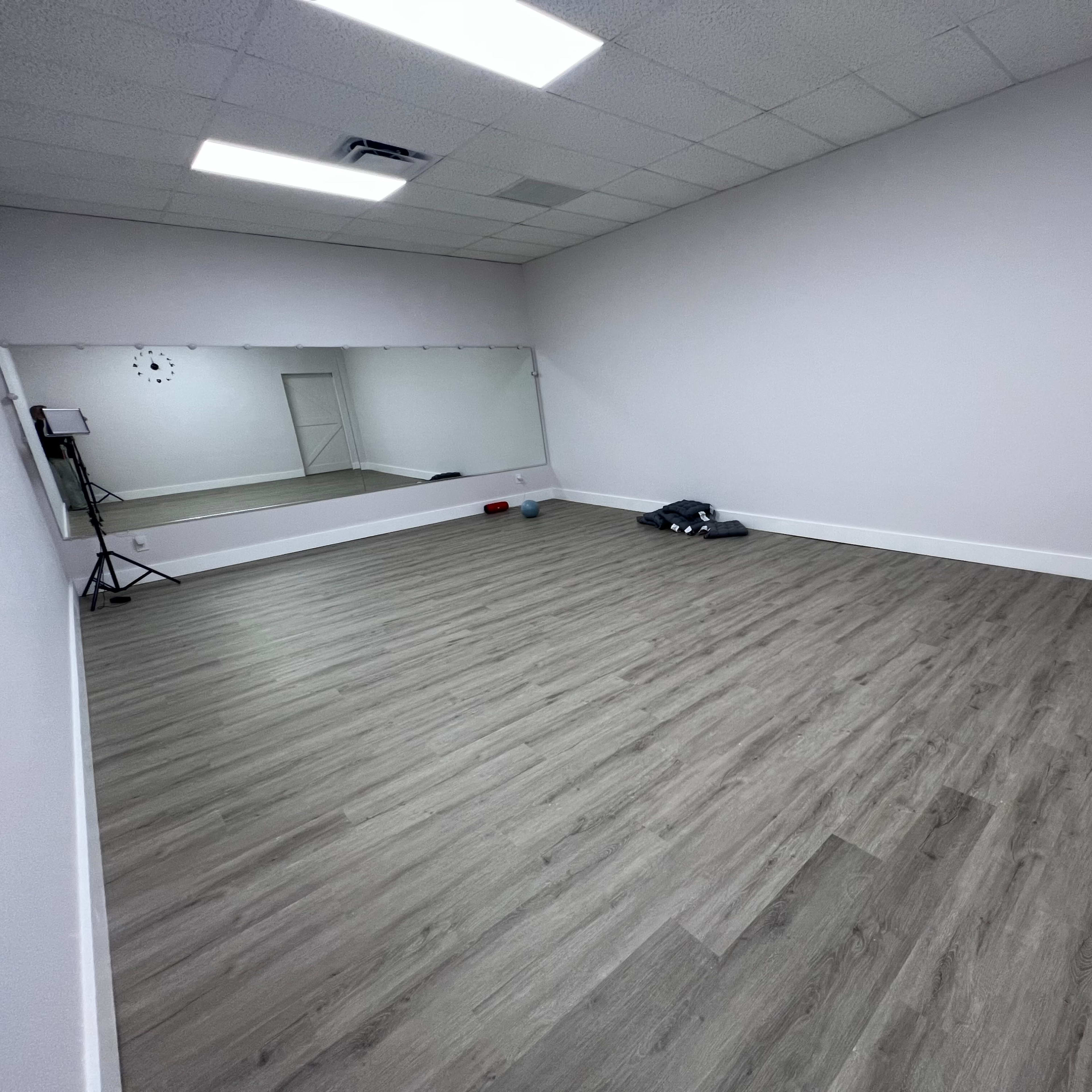 A spacious, empty room with wooden flooring and a large mirror on one wall.