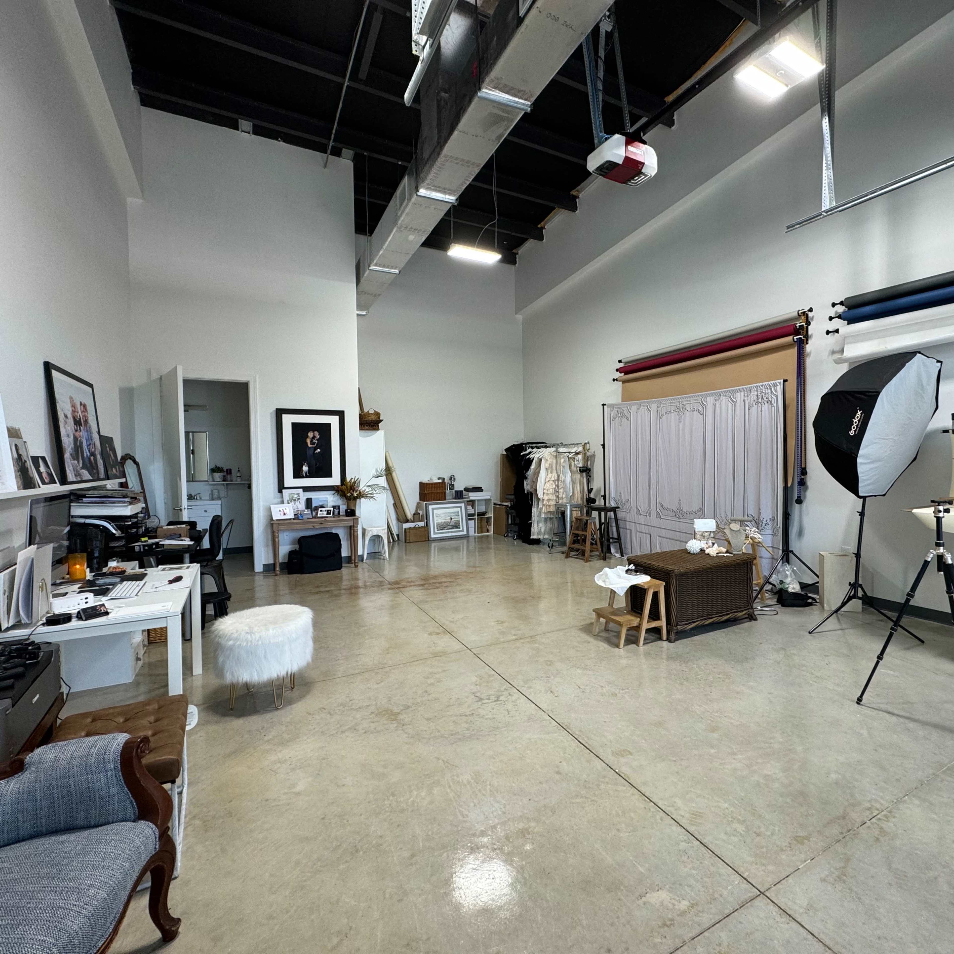 A spacious photo studio with various props, backdrops, and lighting equipment set up along one wall.