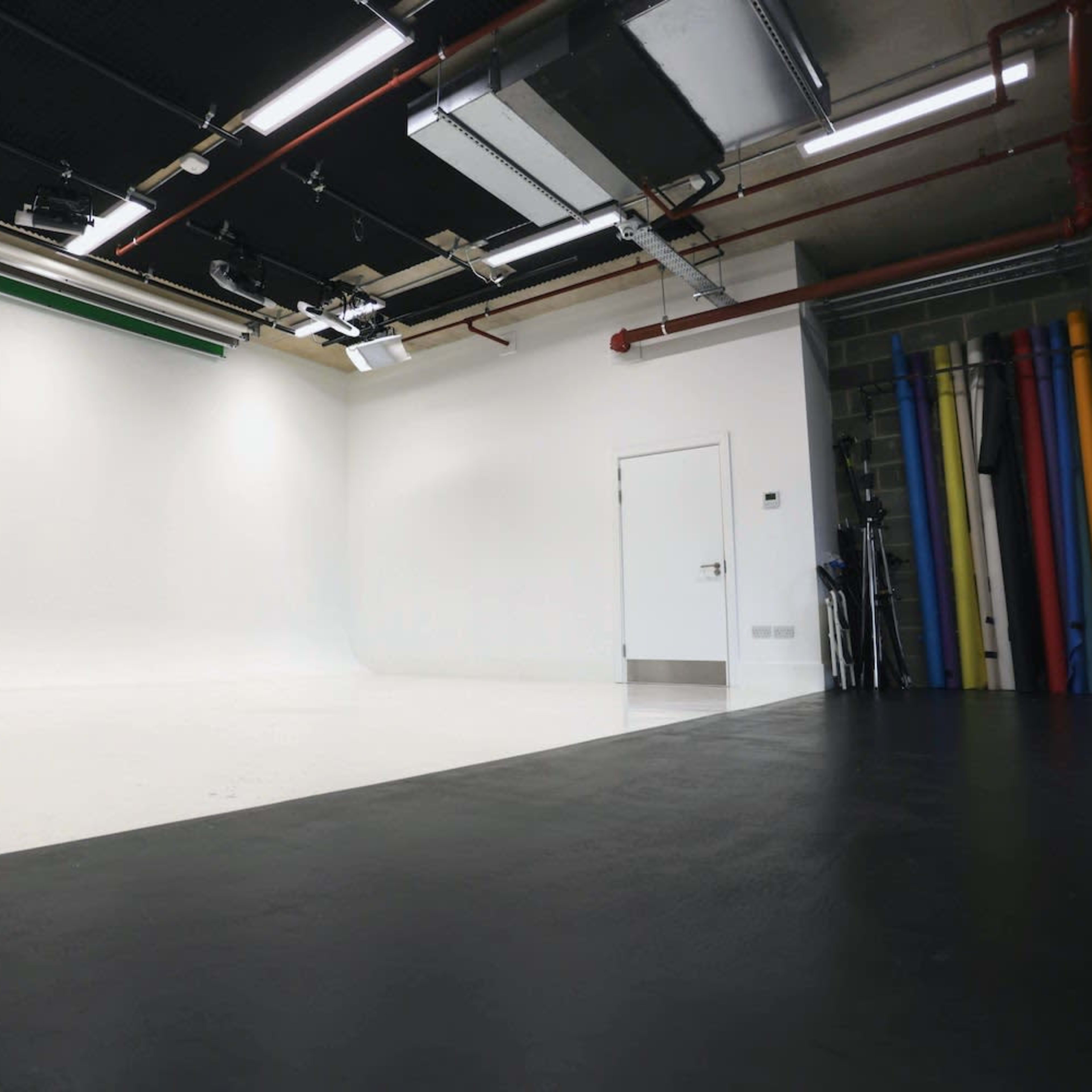 A minimalistic studio space with a white backdrop, a door, and colorful backdrop rolls arranged against a wall.