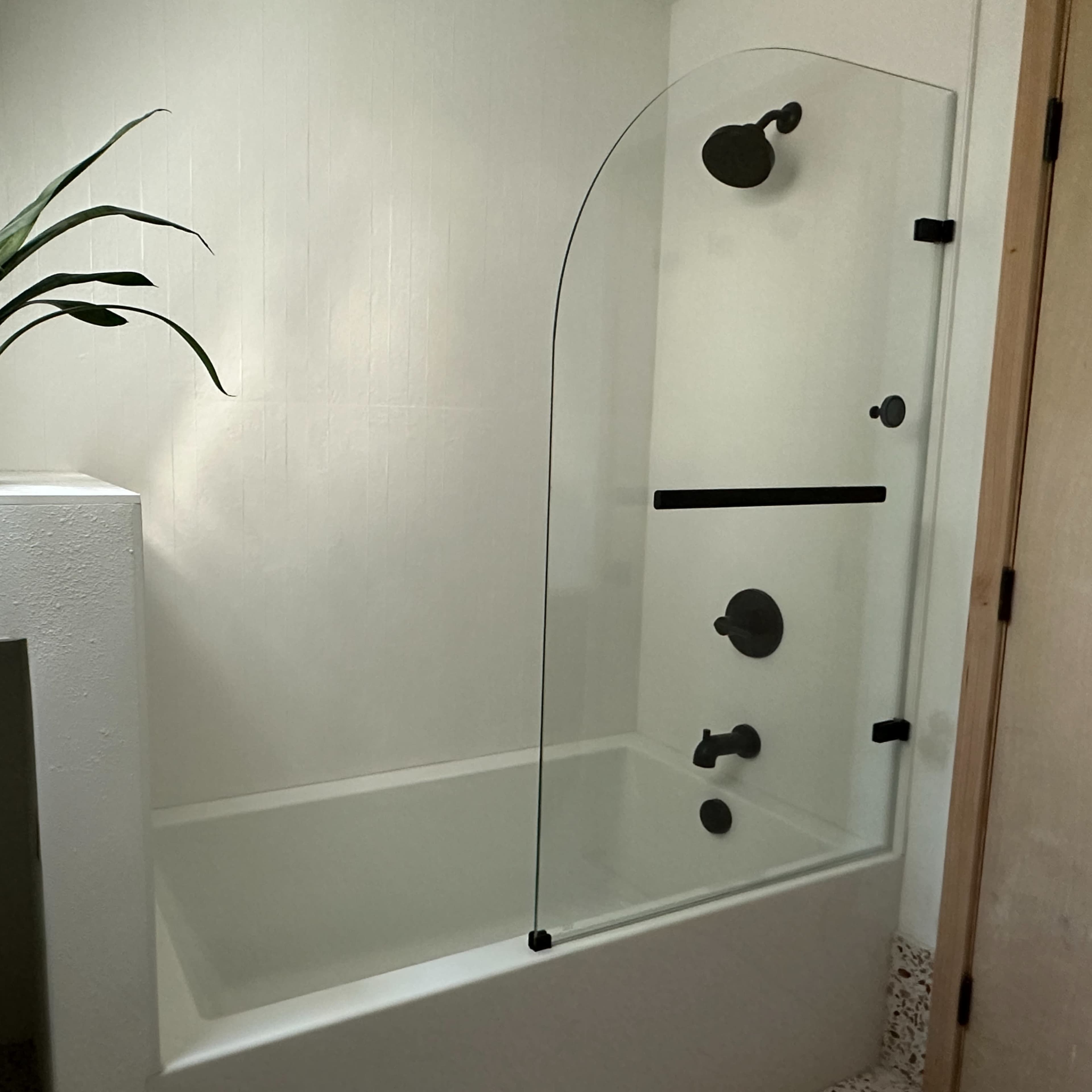 A modern bathroom featuring a glass shower enclosure above a bathtub, complemented by a potted plant on the ledge.