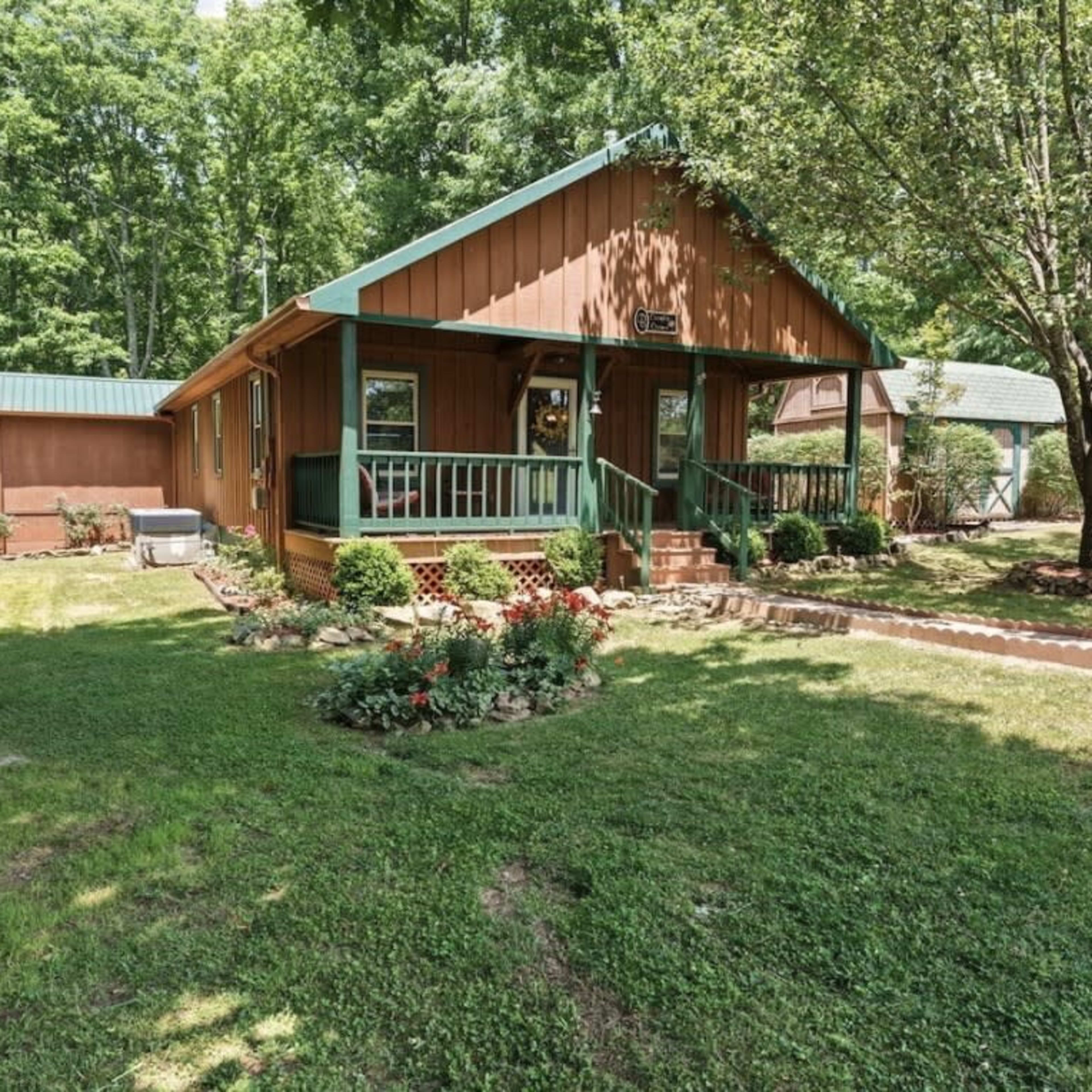A brown wooden house with a green roof, surrounded by a green lawn and trees.