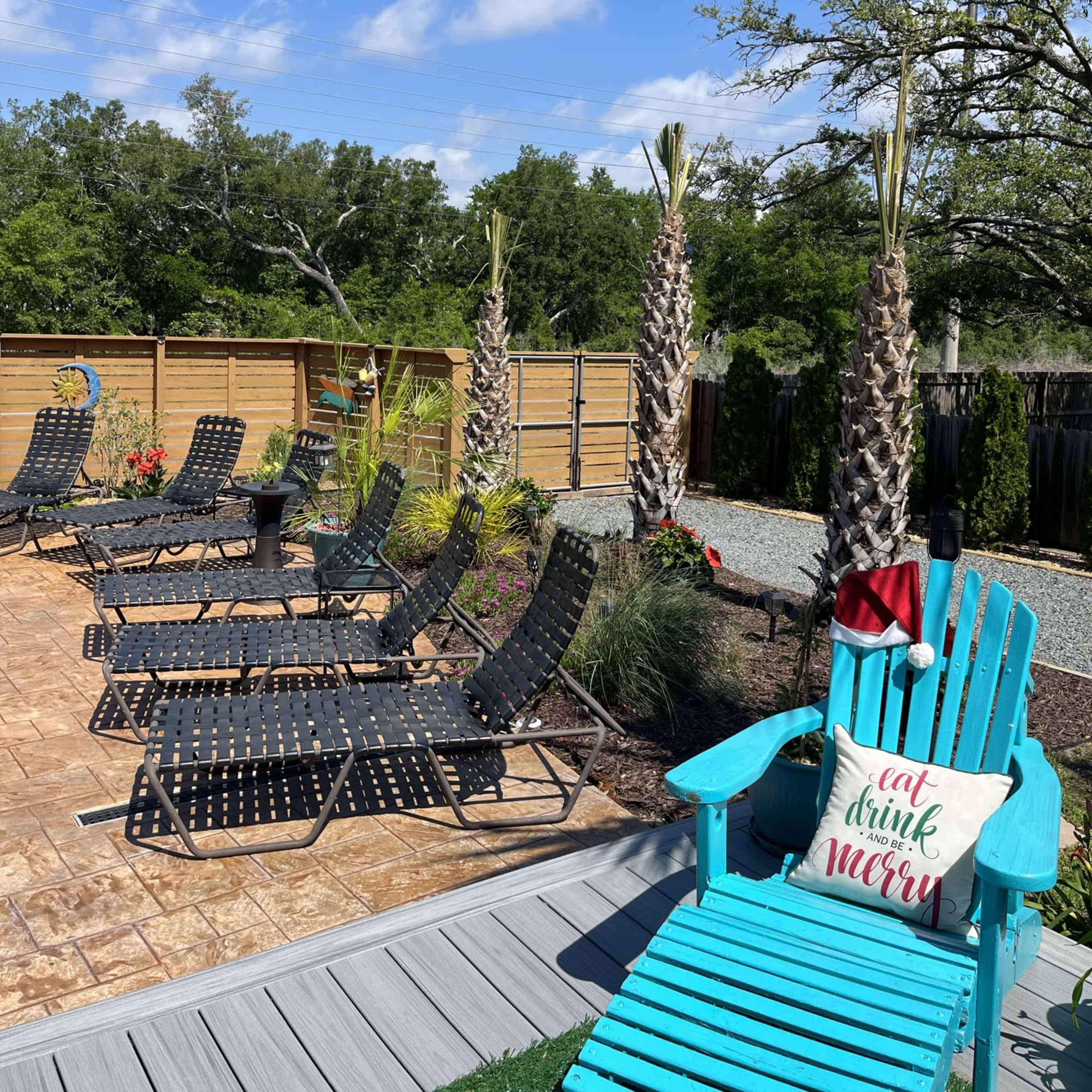 A poolside area with black lounge chairs, decorative plants, and two palm trees under a clear blue sky.