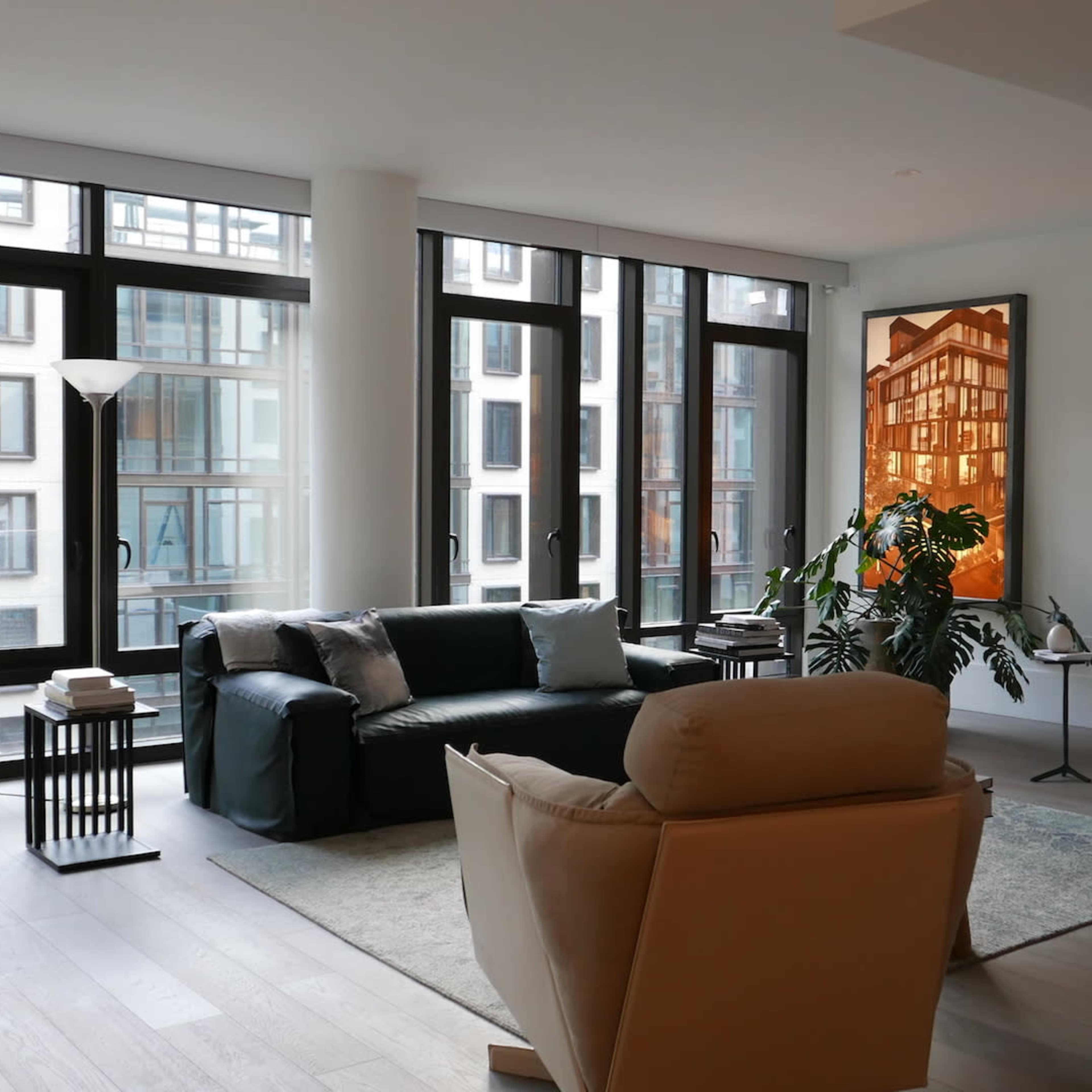 A spacious living room features large windows, modern furniture, and two pieces of artwork on the walls.