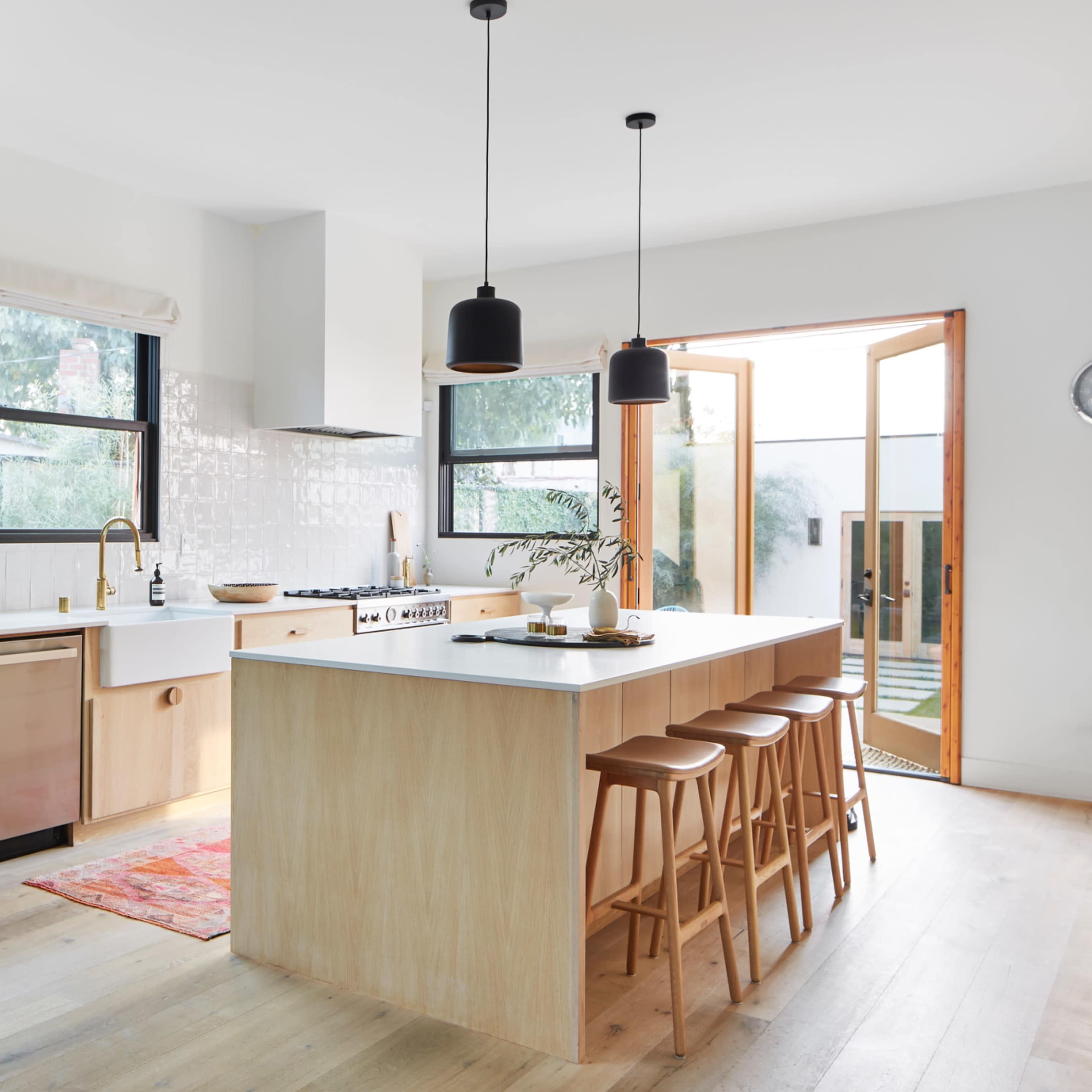 A modern kitchen features a large island with bar stools, wooden cabinetry, and an open doorway leading to an outdoor area.