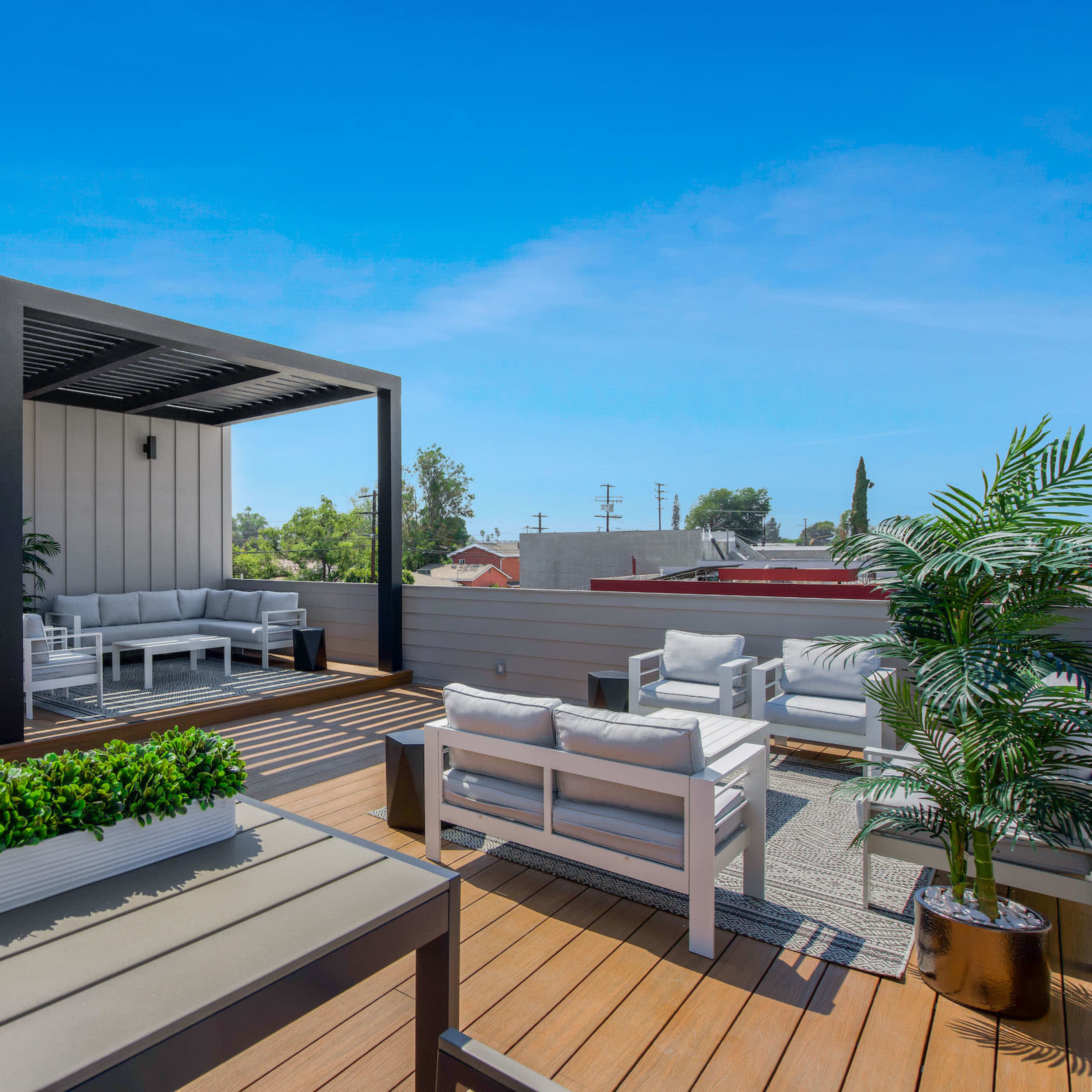 A modern rooftop terrace featuring seating areas, planters, and a pergola against a clear blue sky.