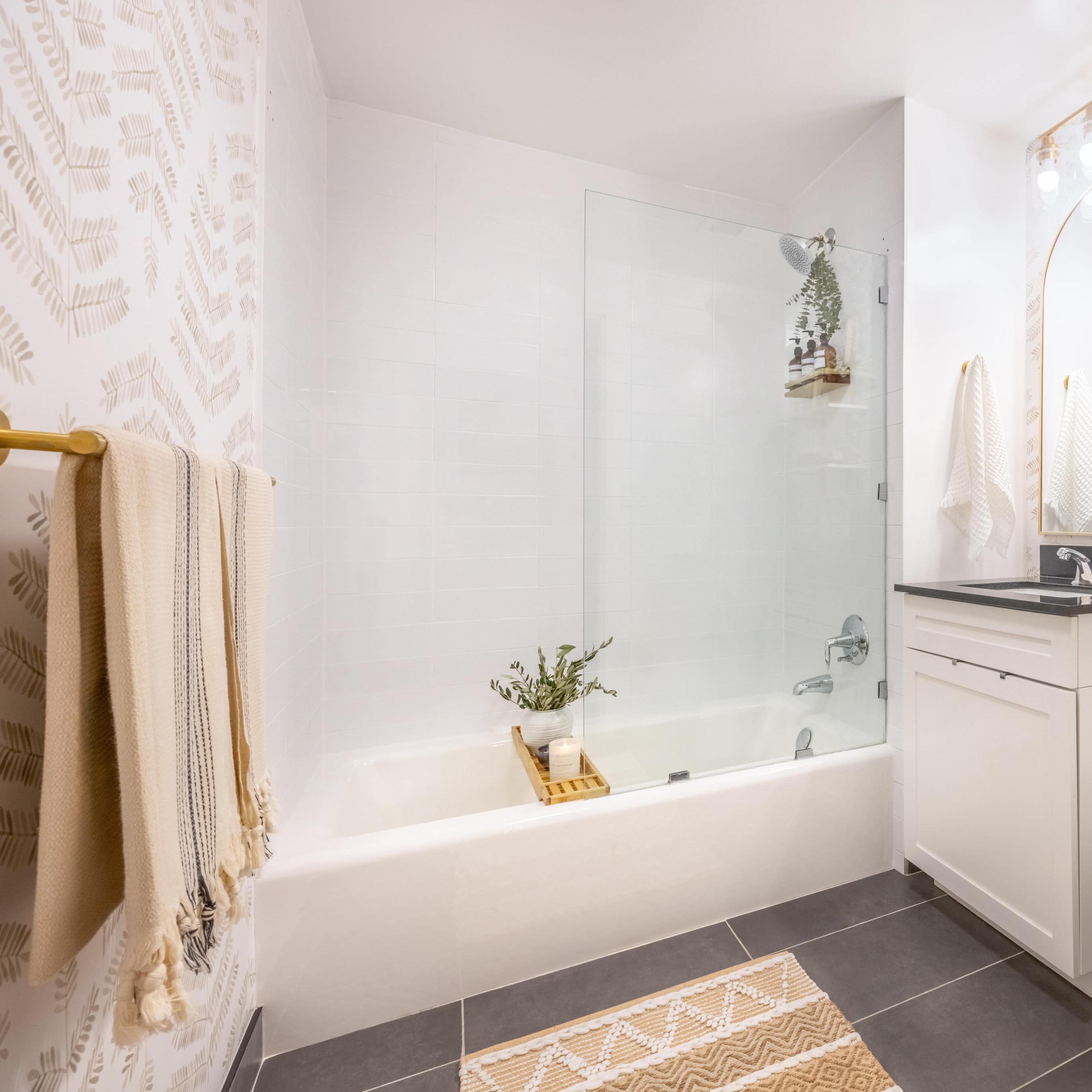 A modern bathroom with a bathtub, a wall-mounted mirror, and a shelf adorned with plants and decorative items.
