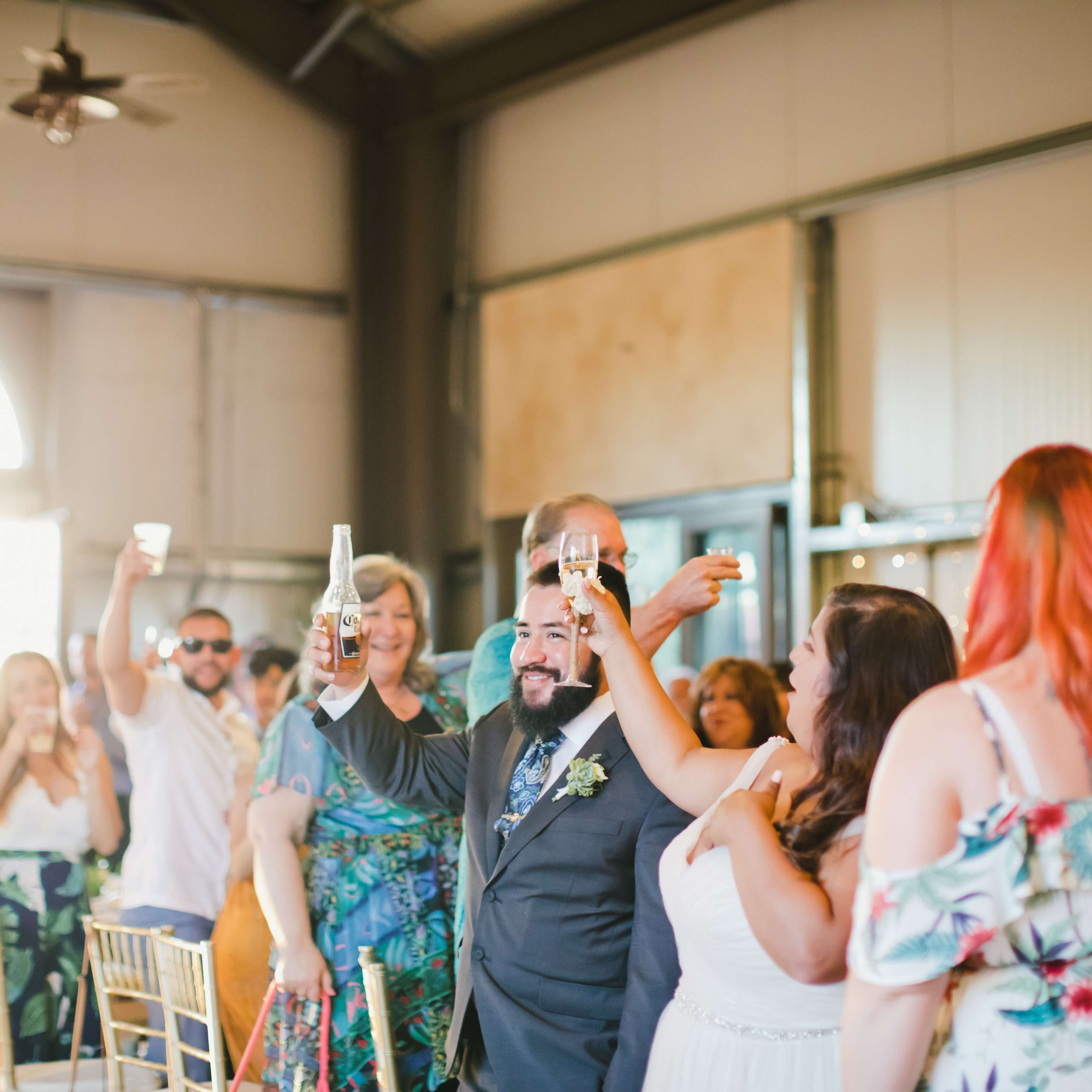 A group of guests raises their glasses in a toast during a celebration at a spacious venue with large windows.