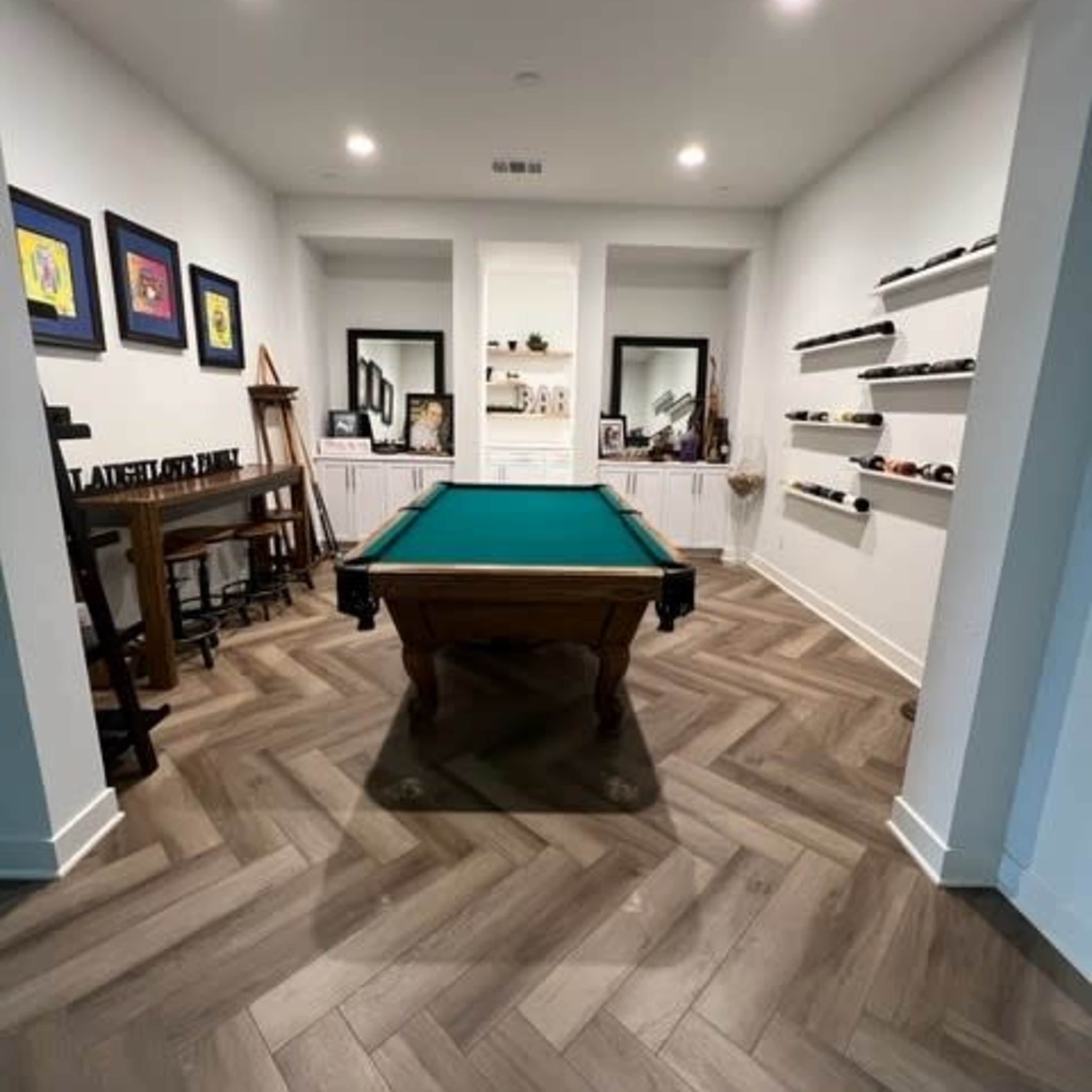 A billiards room featuring a green pool table at its center, surrounded by shelves and artwork on the walls.