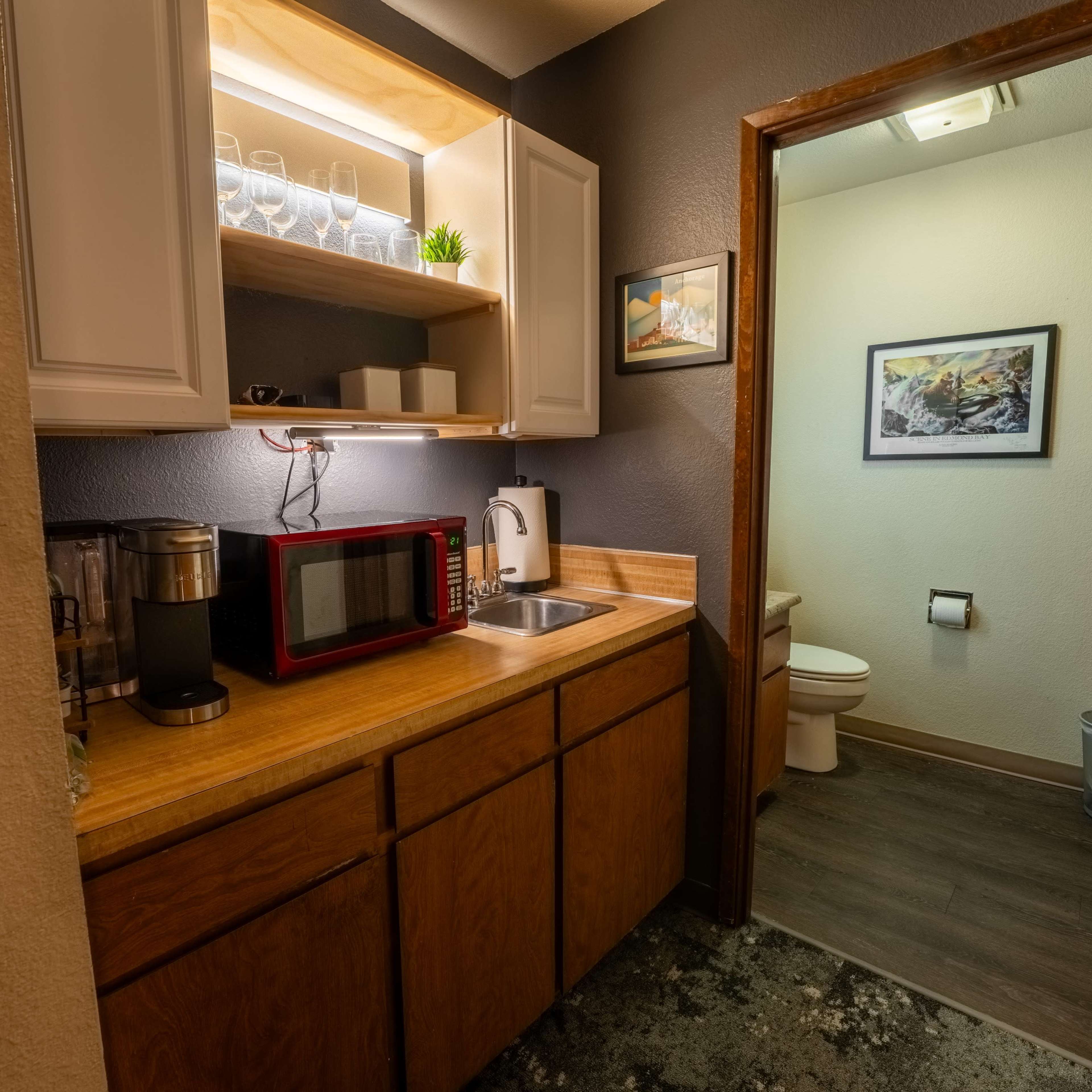A small kitchenette with a microwave, coffee maker, and a bathroom entrance in a compact space.