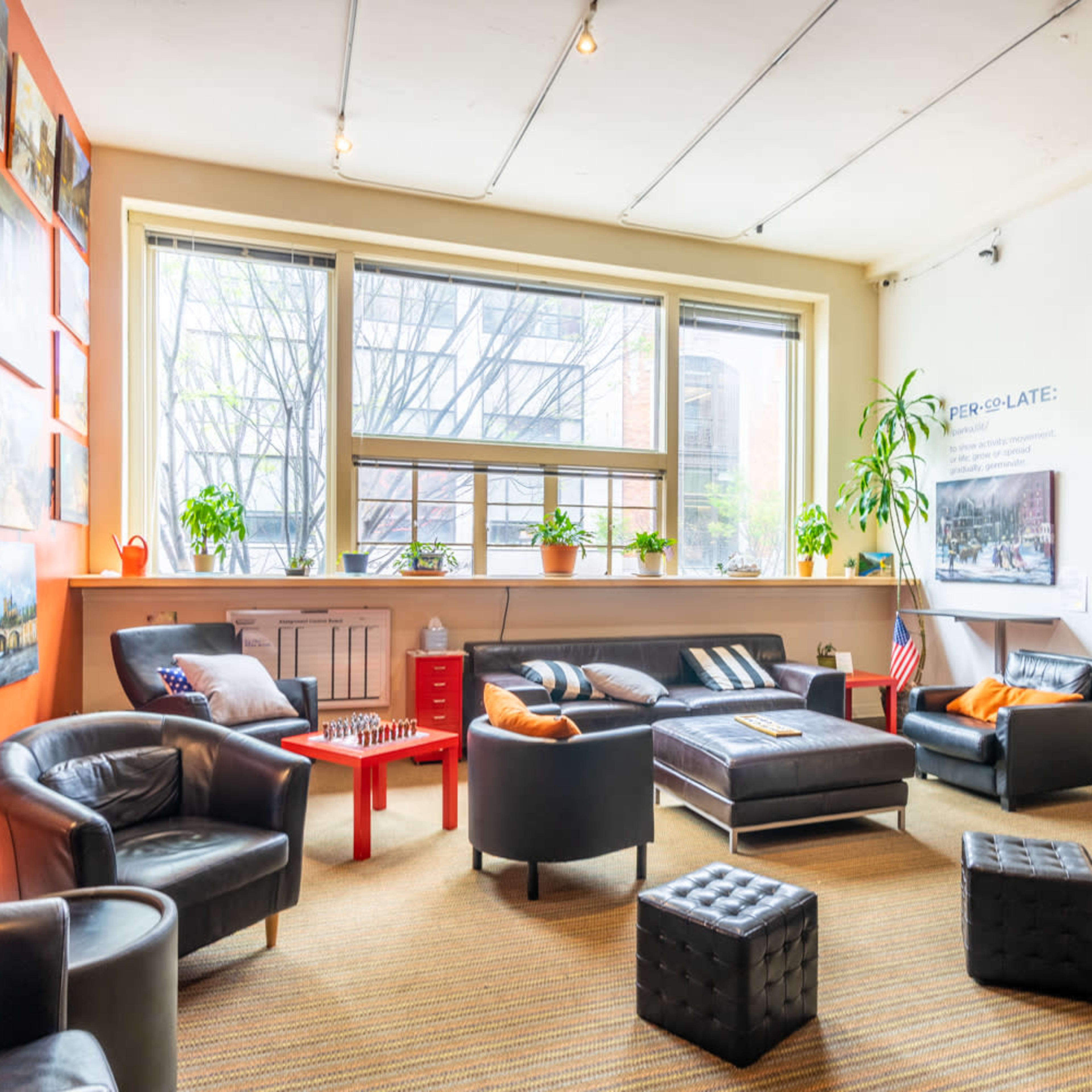 A modern lounge area with leather furniture, a low coffee table, potted plants, and large windows letting in natural light.