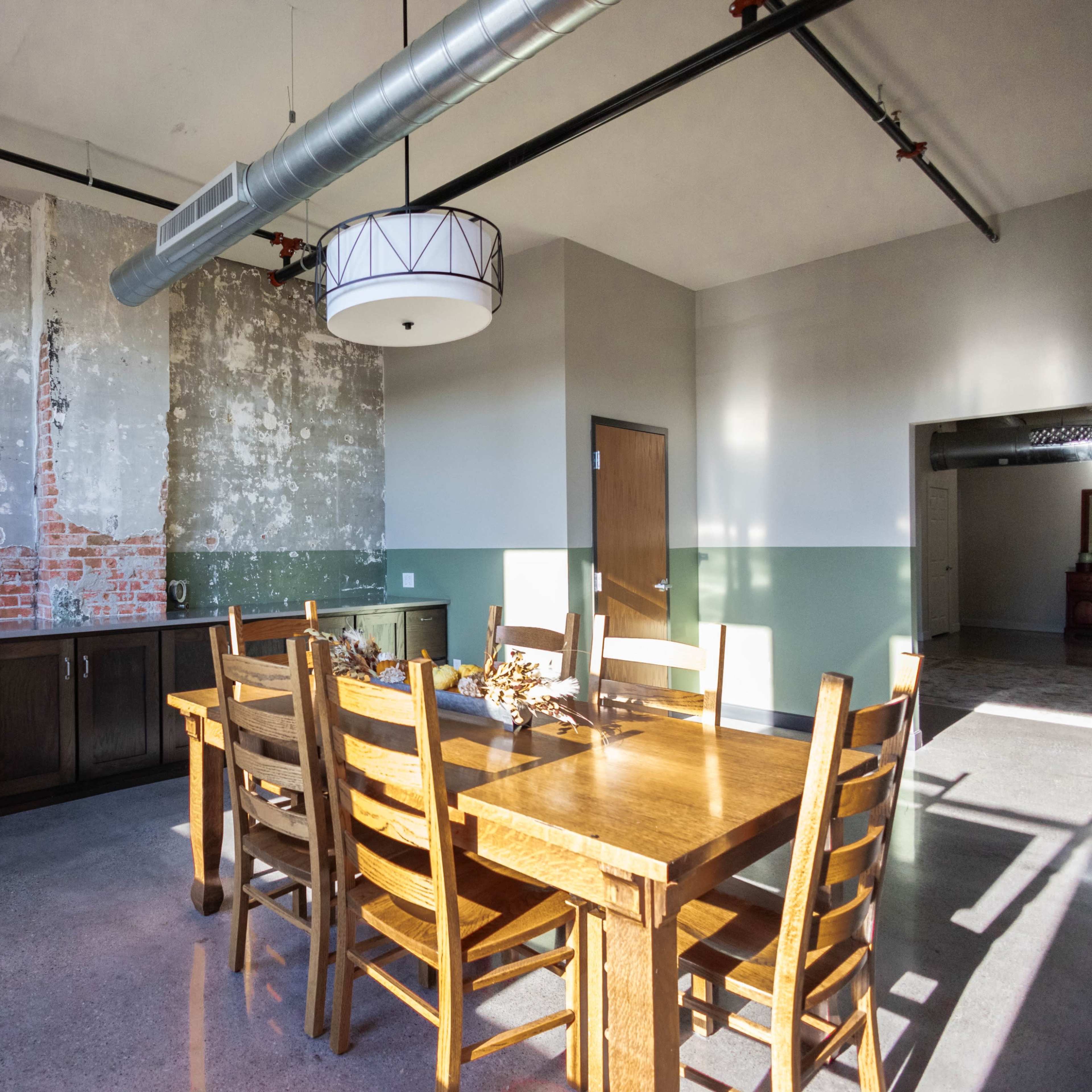 A dining area with a wooden table and chairs, featuring a partially exposed brick wall and a modern light fixture.