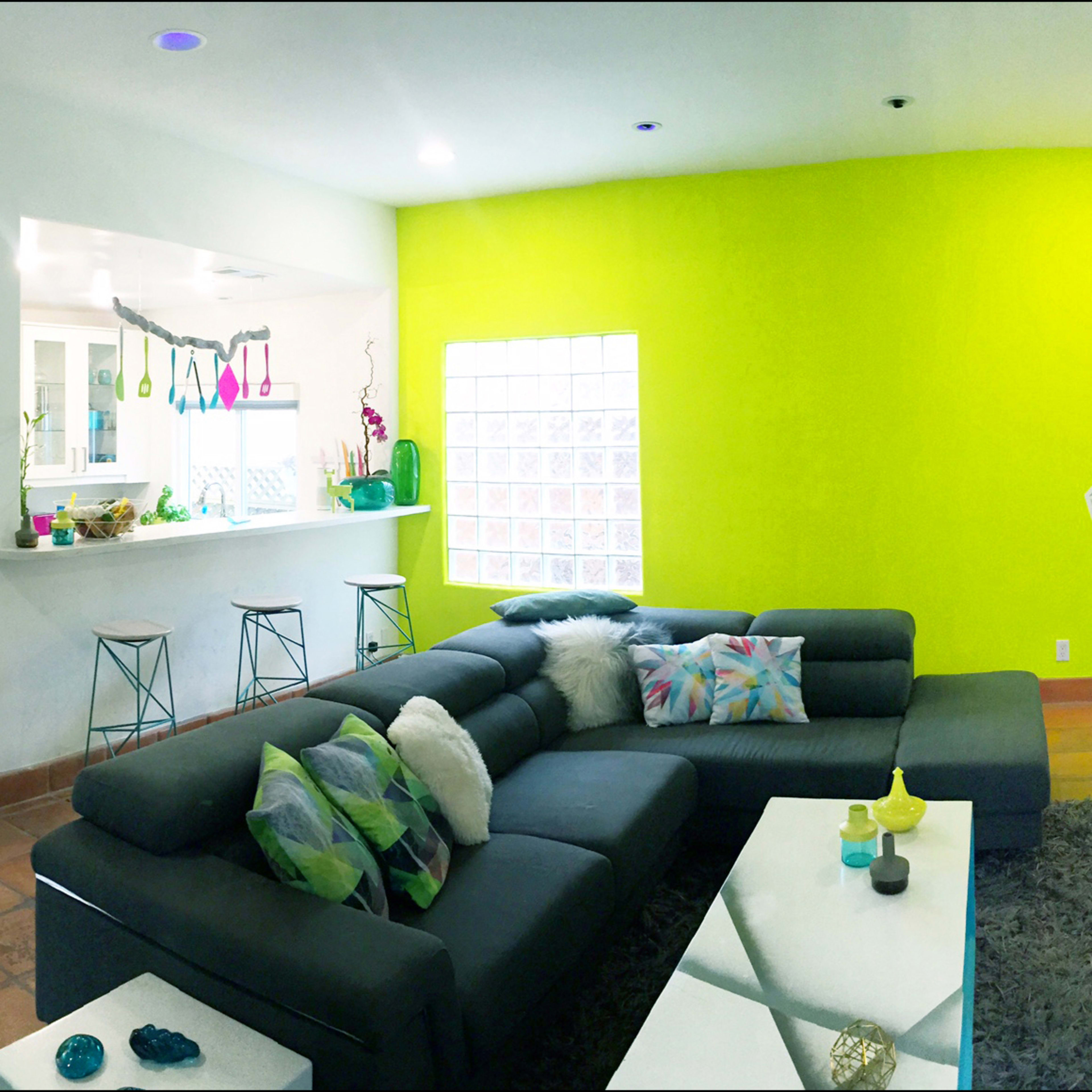 A brightly colored open-concept living space featuring a black sectional sofa, an island bar with stools, and vibrant green and blue accents on the walls.