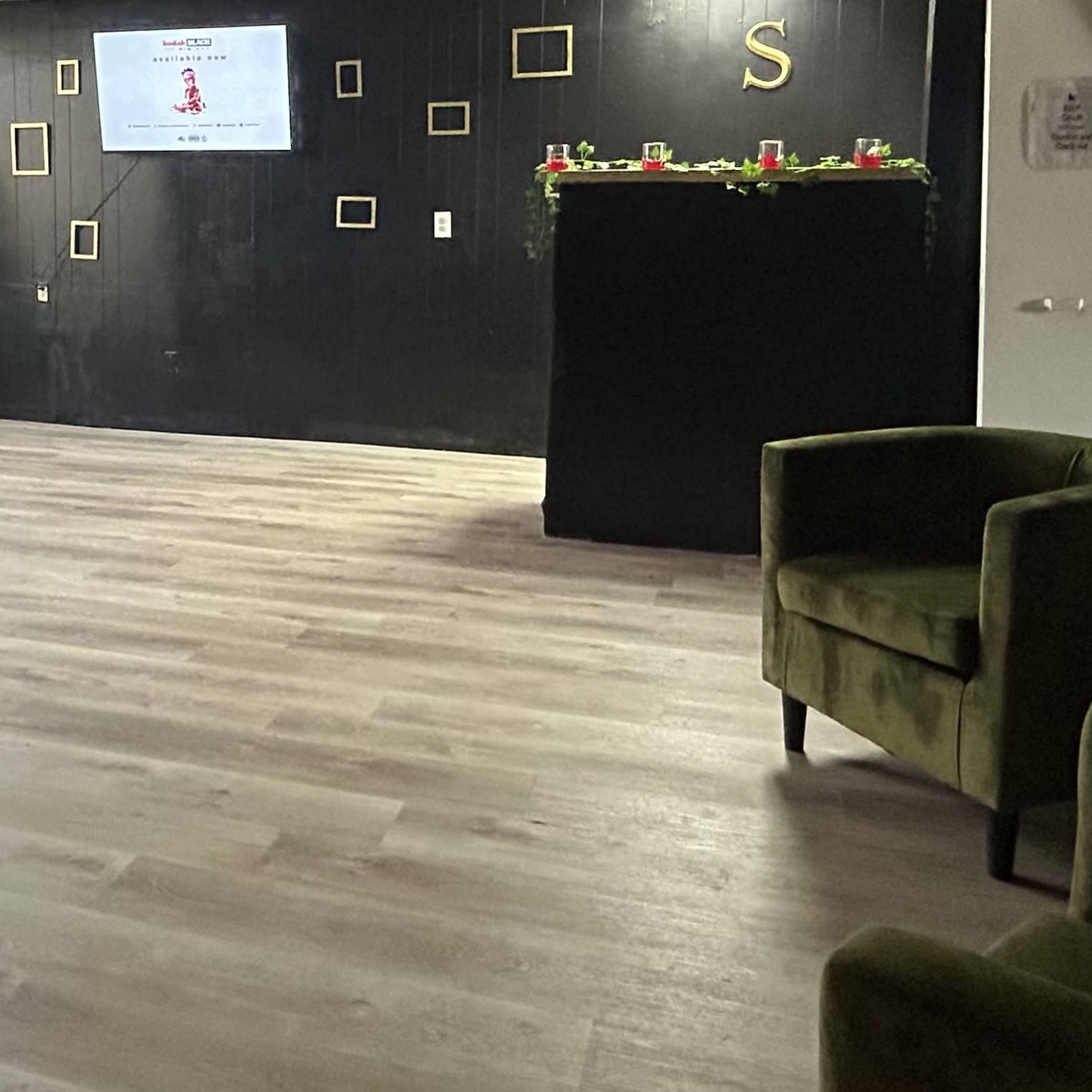 A spacious interior with dark walls, wooden flooring, a reception area, and green plants.