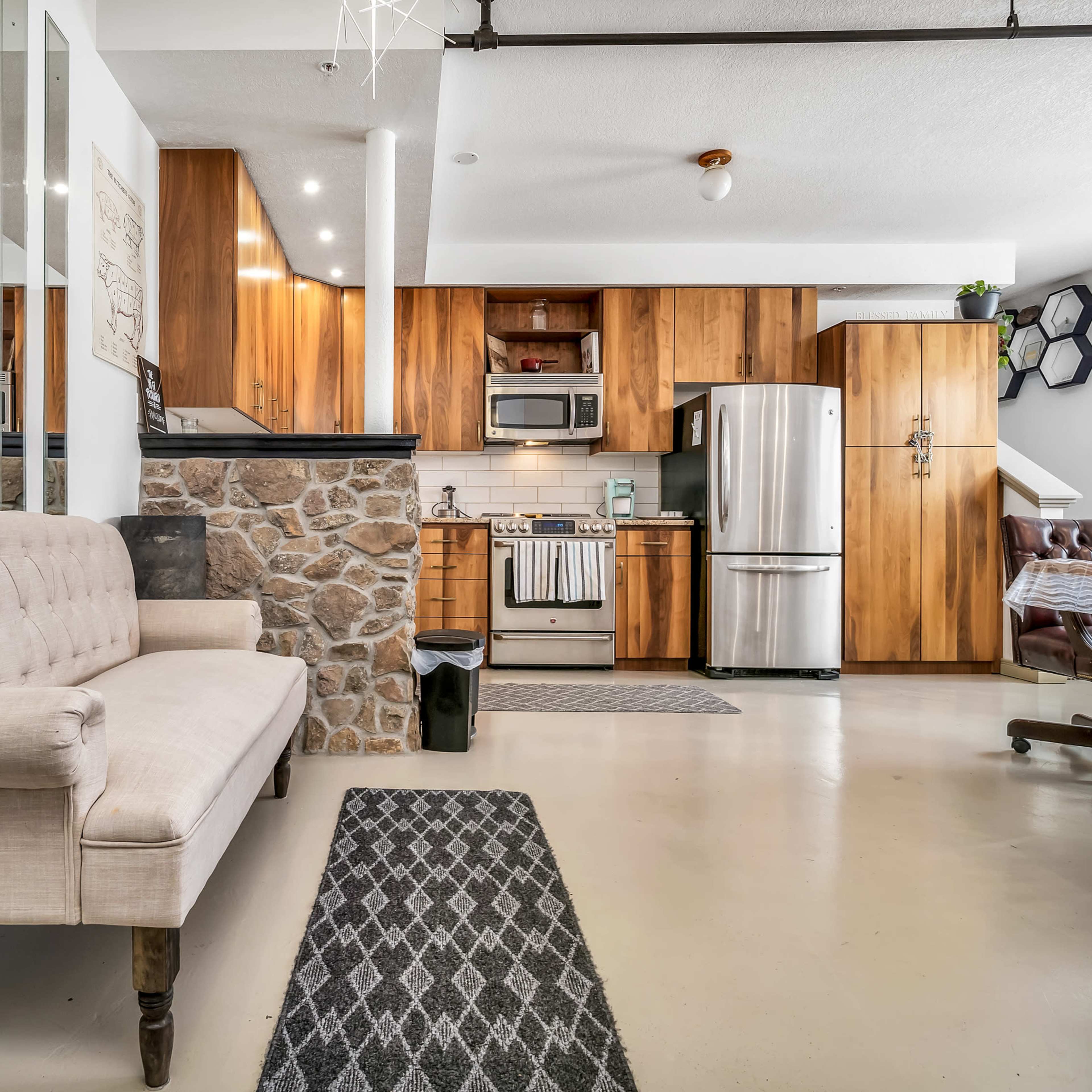 A modern kitchen and living area featuring wooden cabinetry, a beige sofa, and a stone accent wall.