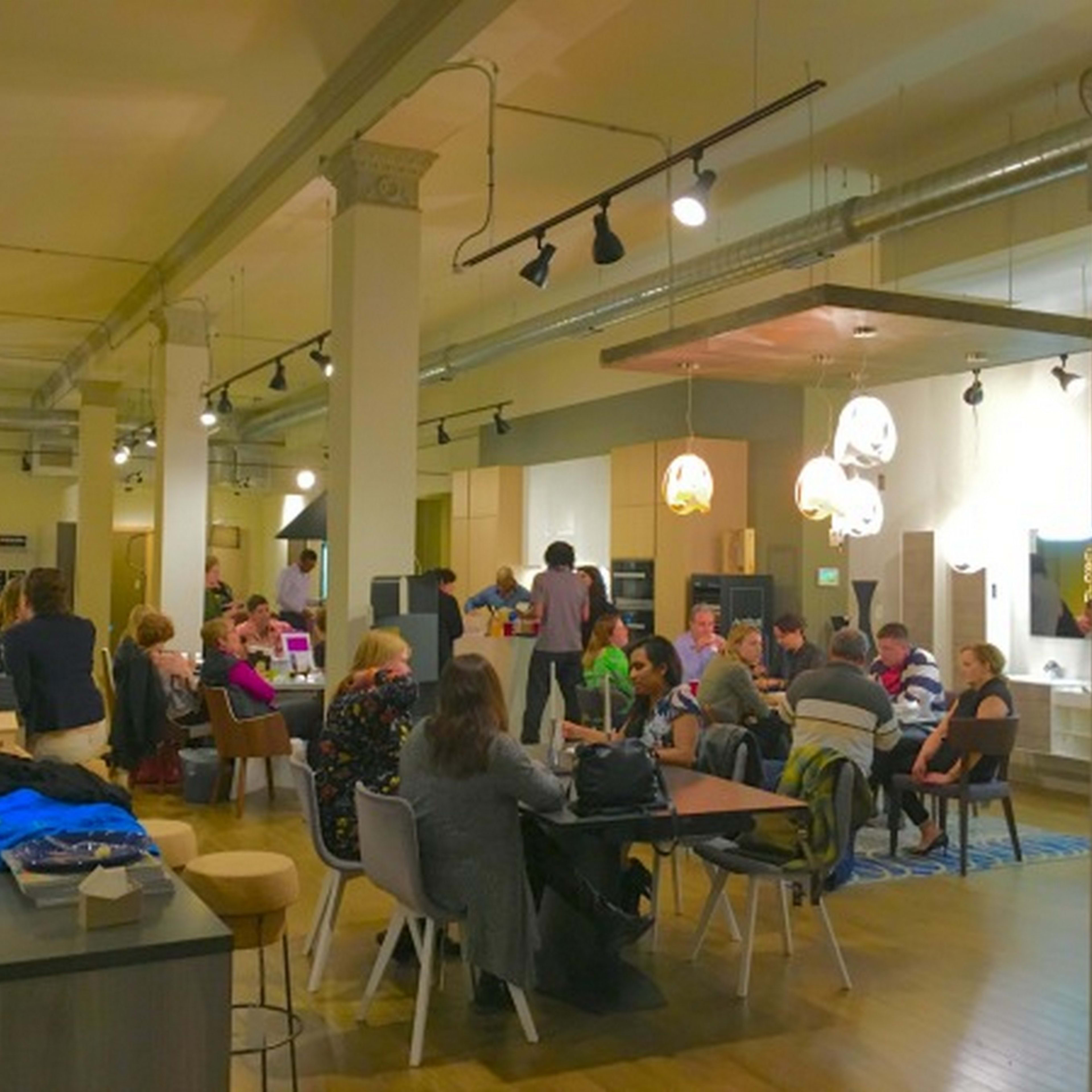 A large, modern workspace features people seated at tables engaged in conversations and activities.