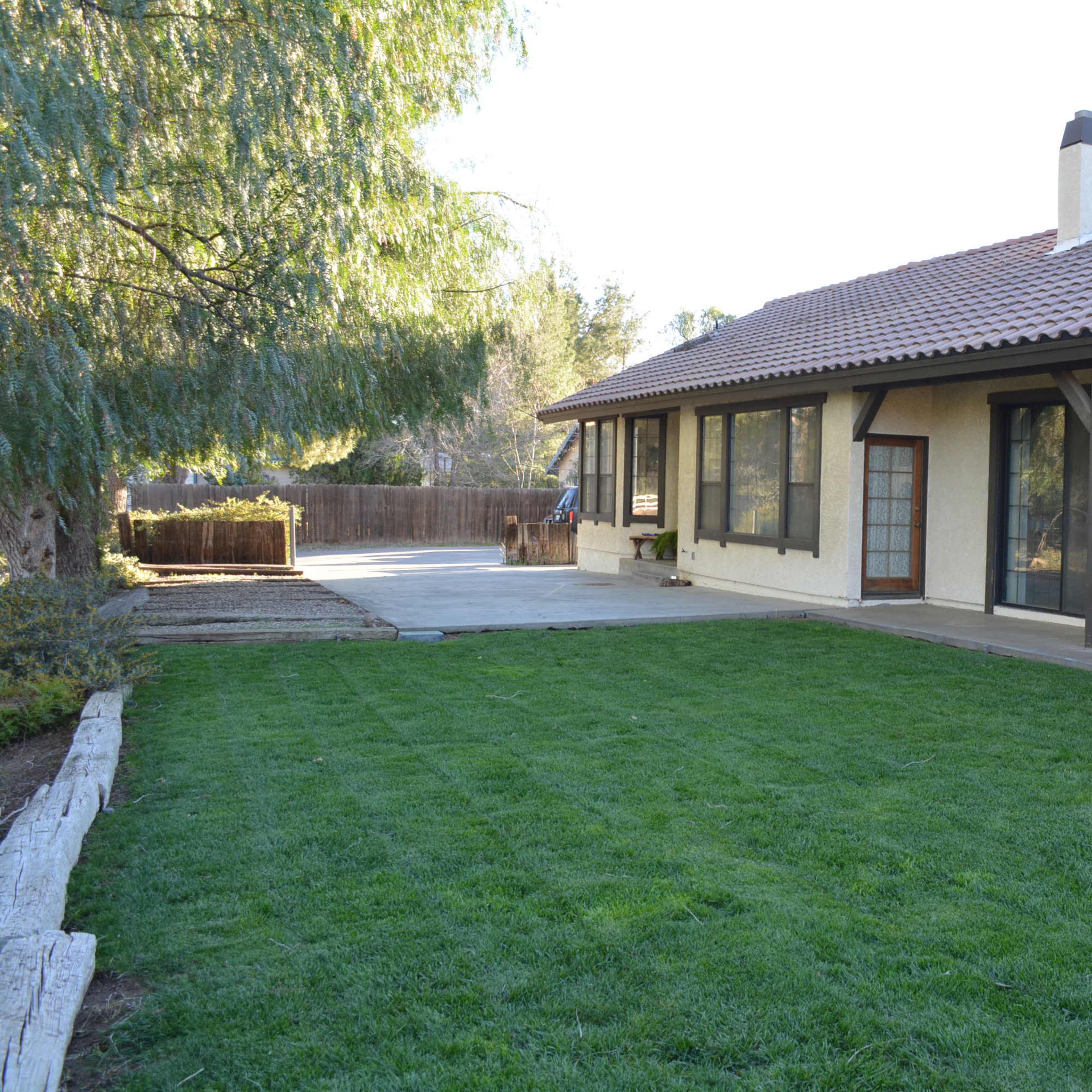 A single-story house with a tiled roof and a landscaped backyard featuring freshly cut grass.