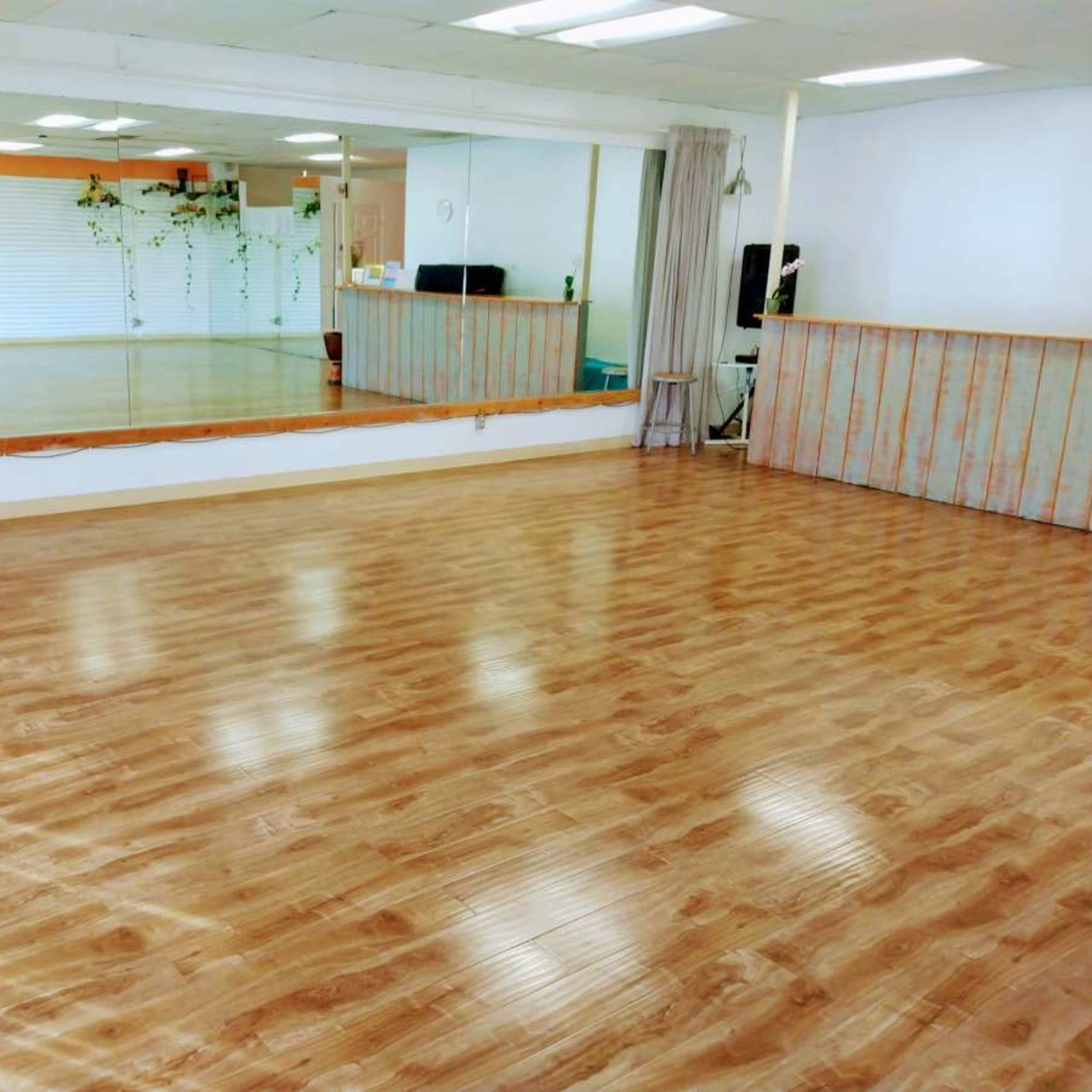 A spacious dance studio featuring a polished wooden floor and a large mirror on one side.
