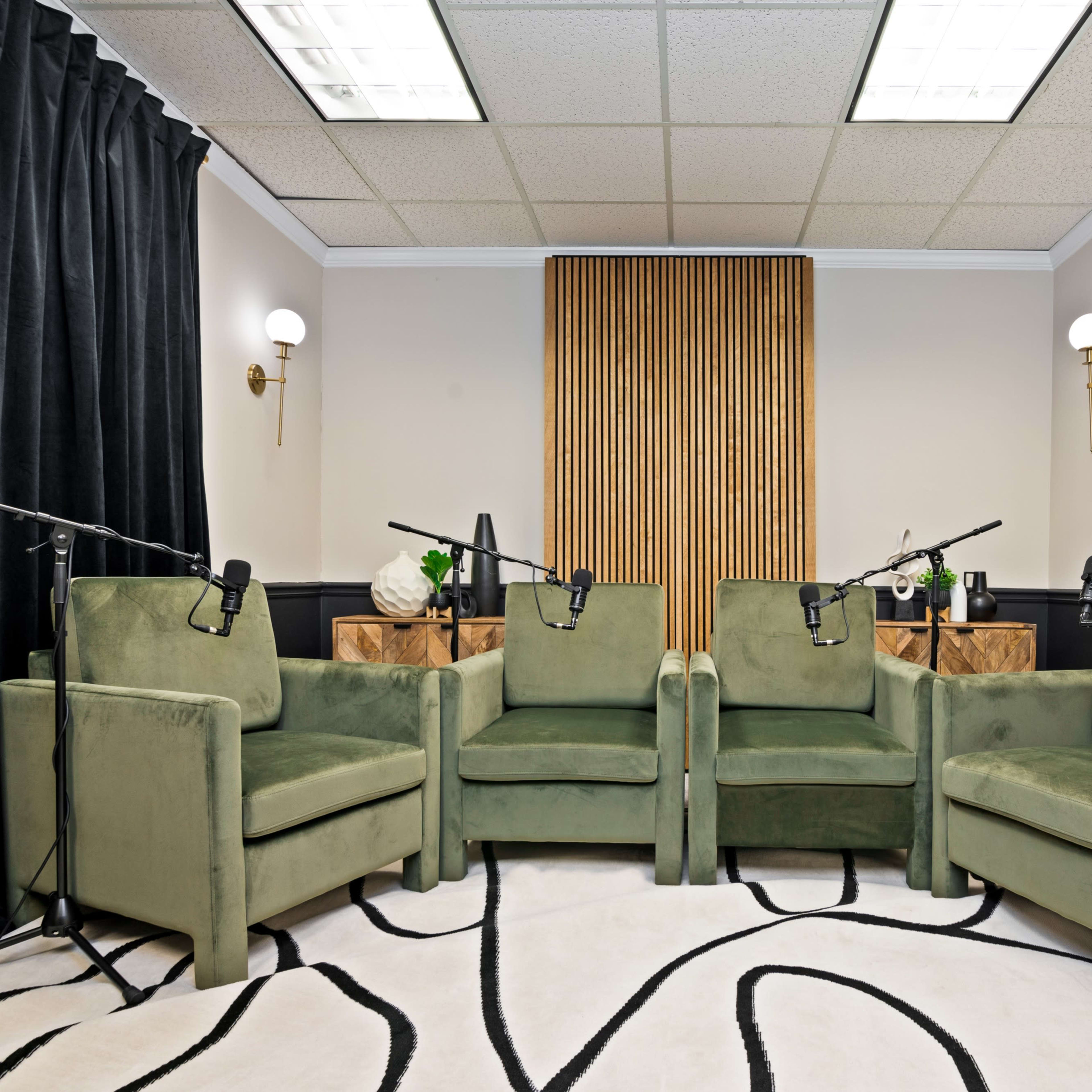 A recording studio features four green chairs arranged around a central space, with microphones positioned on stands in front of each chair.