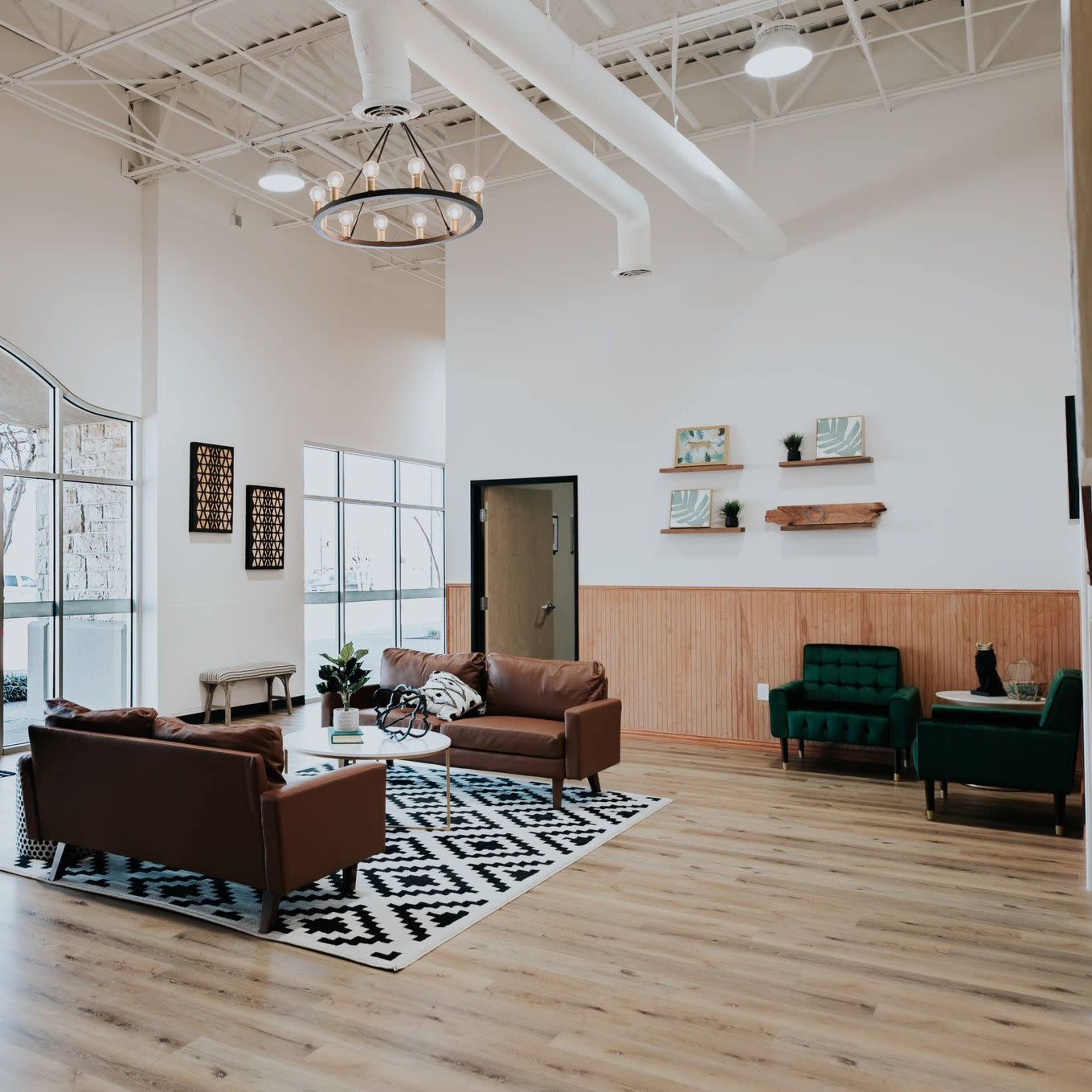 A modern lounge area with brown leather sofas, green armchairs, a patterned rug, and wooden wall accents.