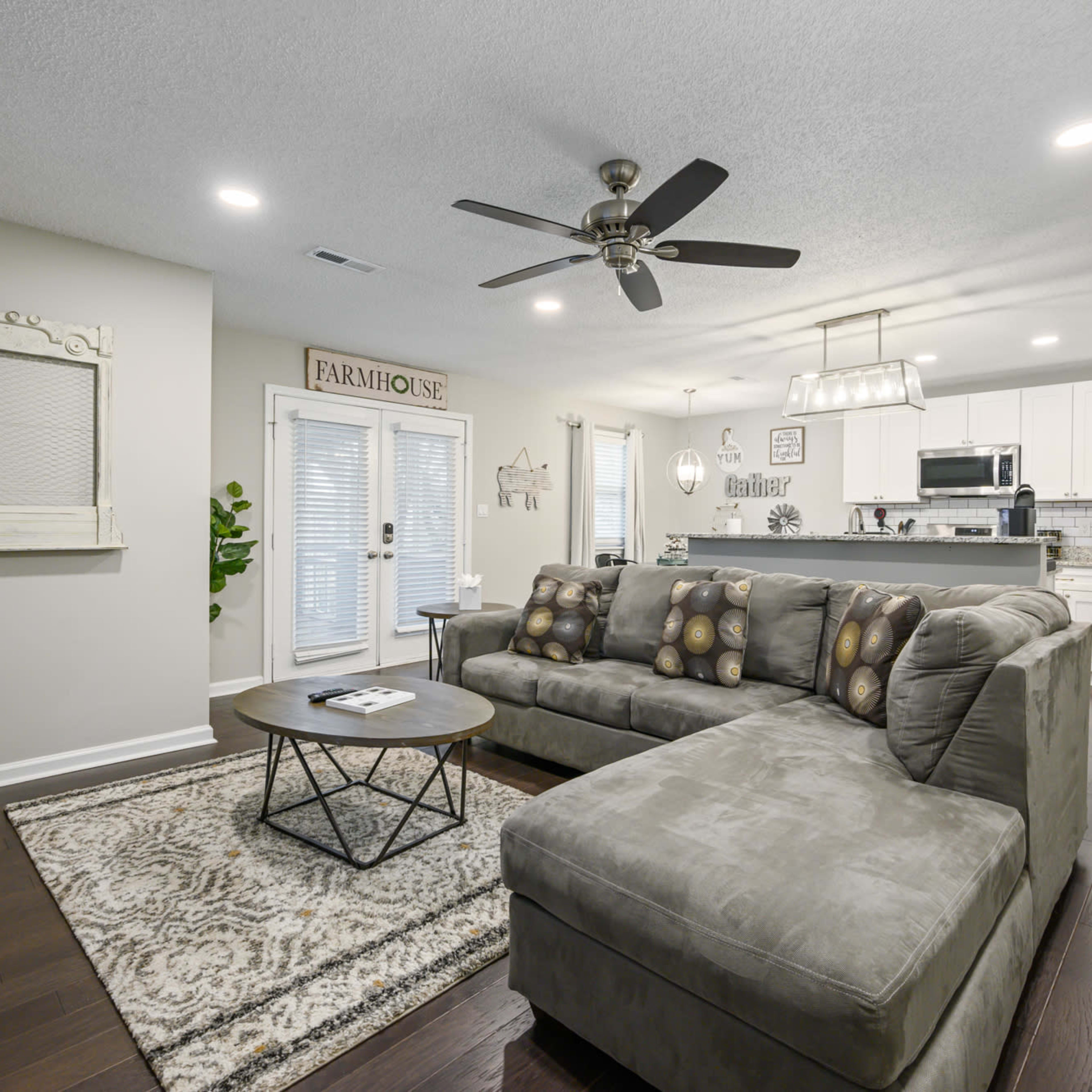 A modern living room featuring a gray sectional sofa, a round coffee table, and a kitchen area visible in the background.