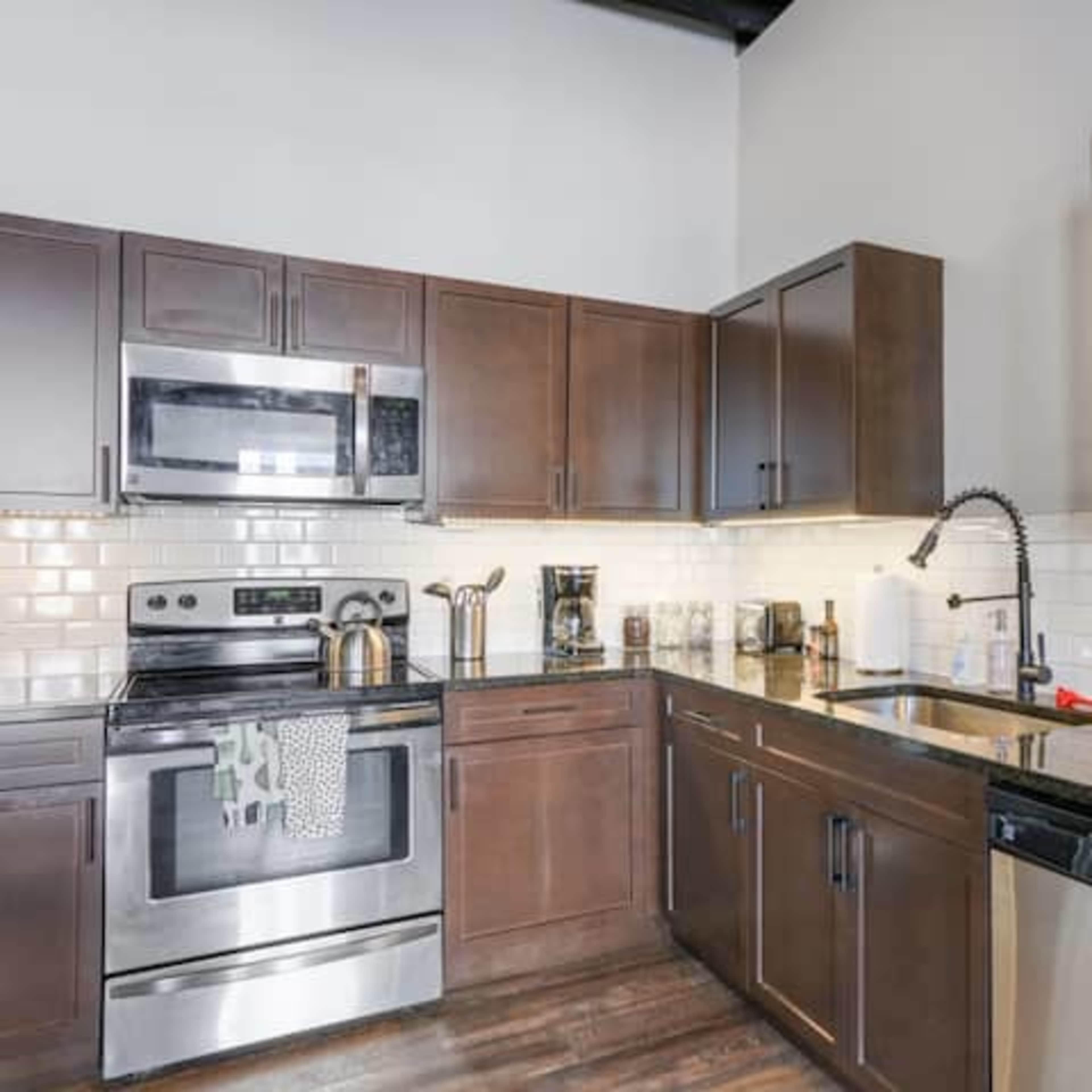 The kitchen features dark wood cabinetry, stainless steel appliances, and a black granite countertop with a tile backsplash.