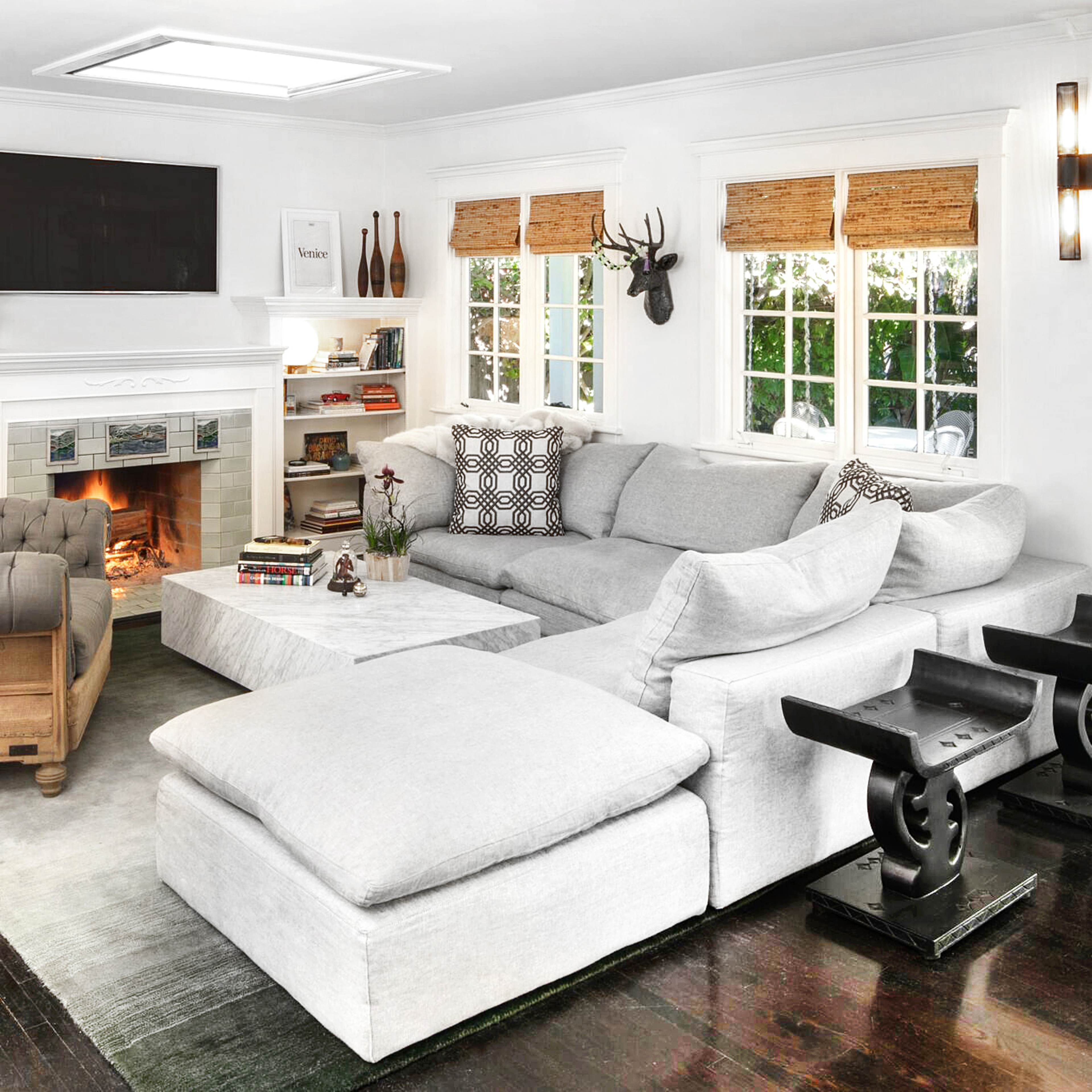 A cozy living room featuring a large gray sectional sofa, a fireplace with a TV above it, and bookshelves filled with decorative items.