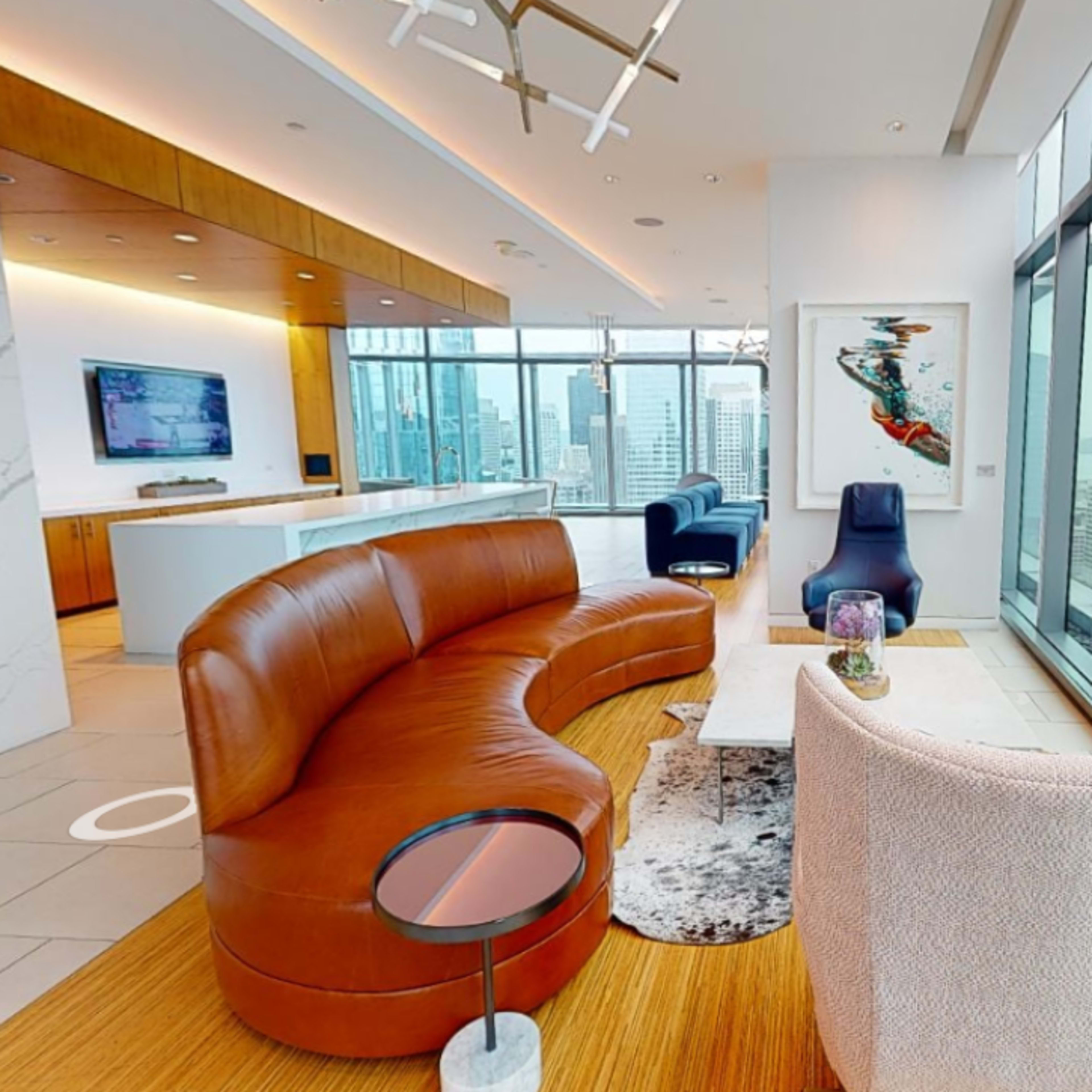 A modern, stylish living space with large windows, a curved leather sofa, and contemporary furniture, overlooking a city skyline.