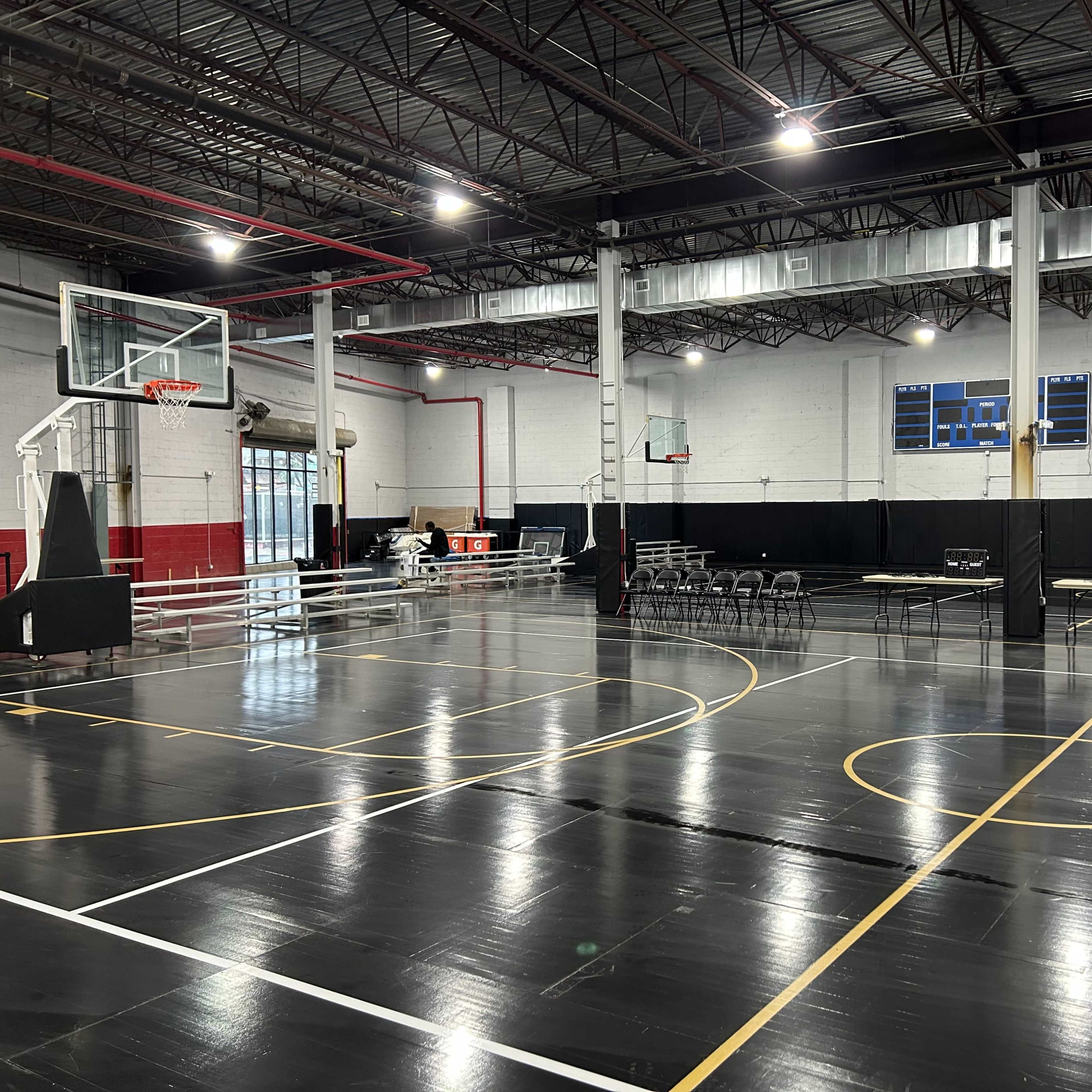 An indoor basketball court with folding chairs and tables set up along one side.