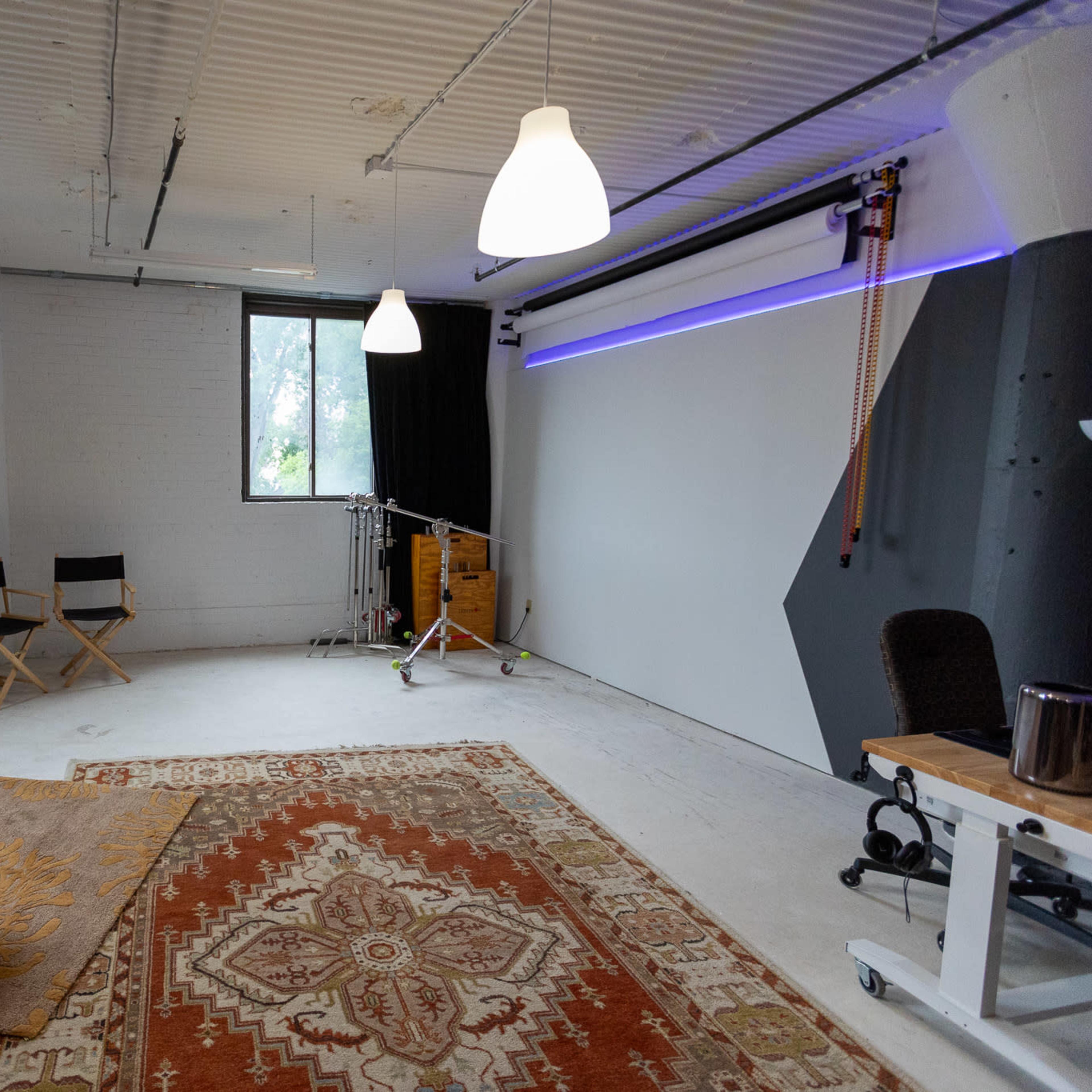 A spacious, minimally furnished studio with two director's chairs, a large area rug, and a backdrop setup against a white wall.
