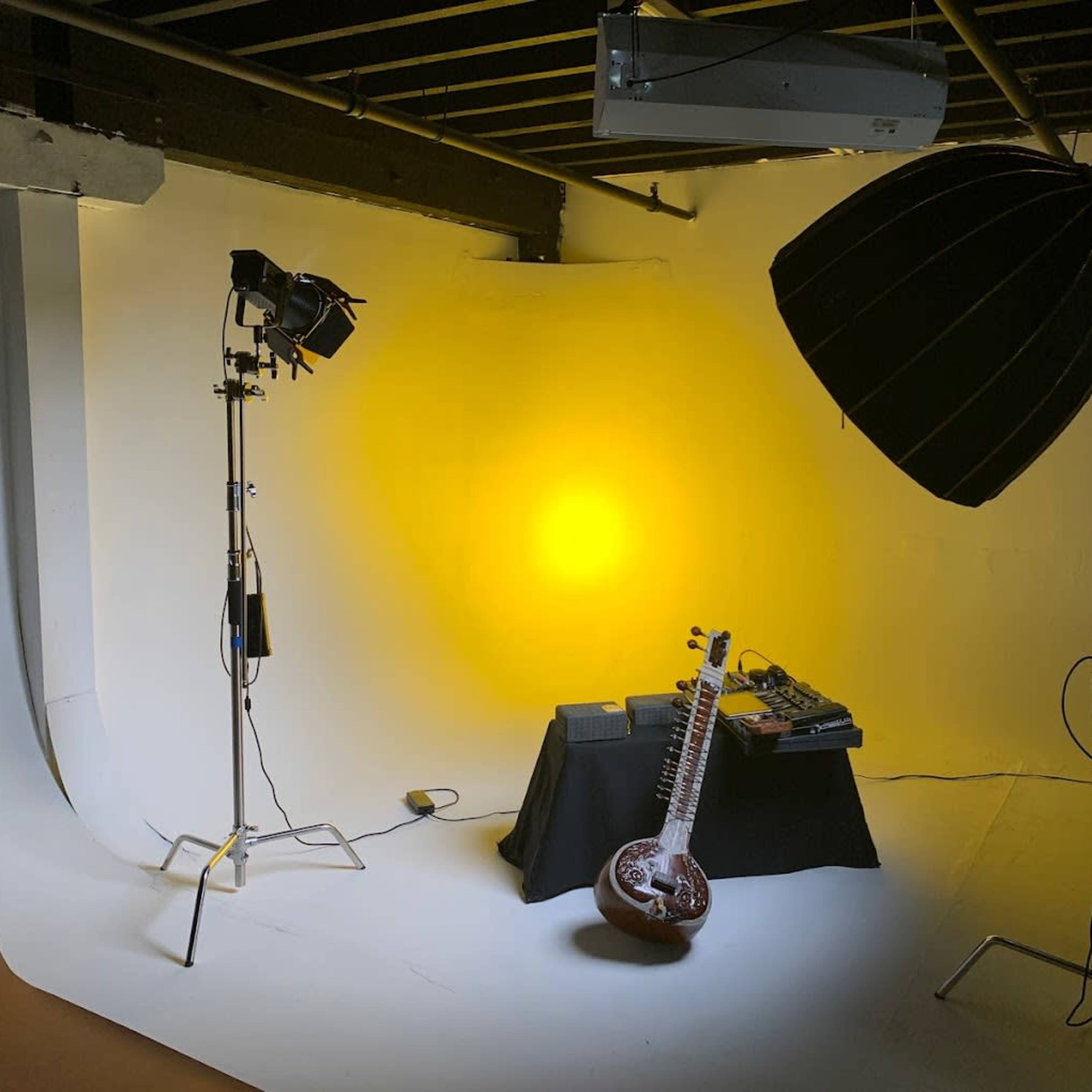 A photography studio setup featuring a sitar placed on a table, accompanied by music equipment, with two light sources illuminating a yellow backdrop.