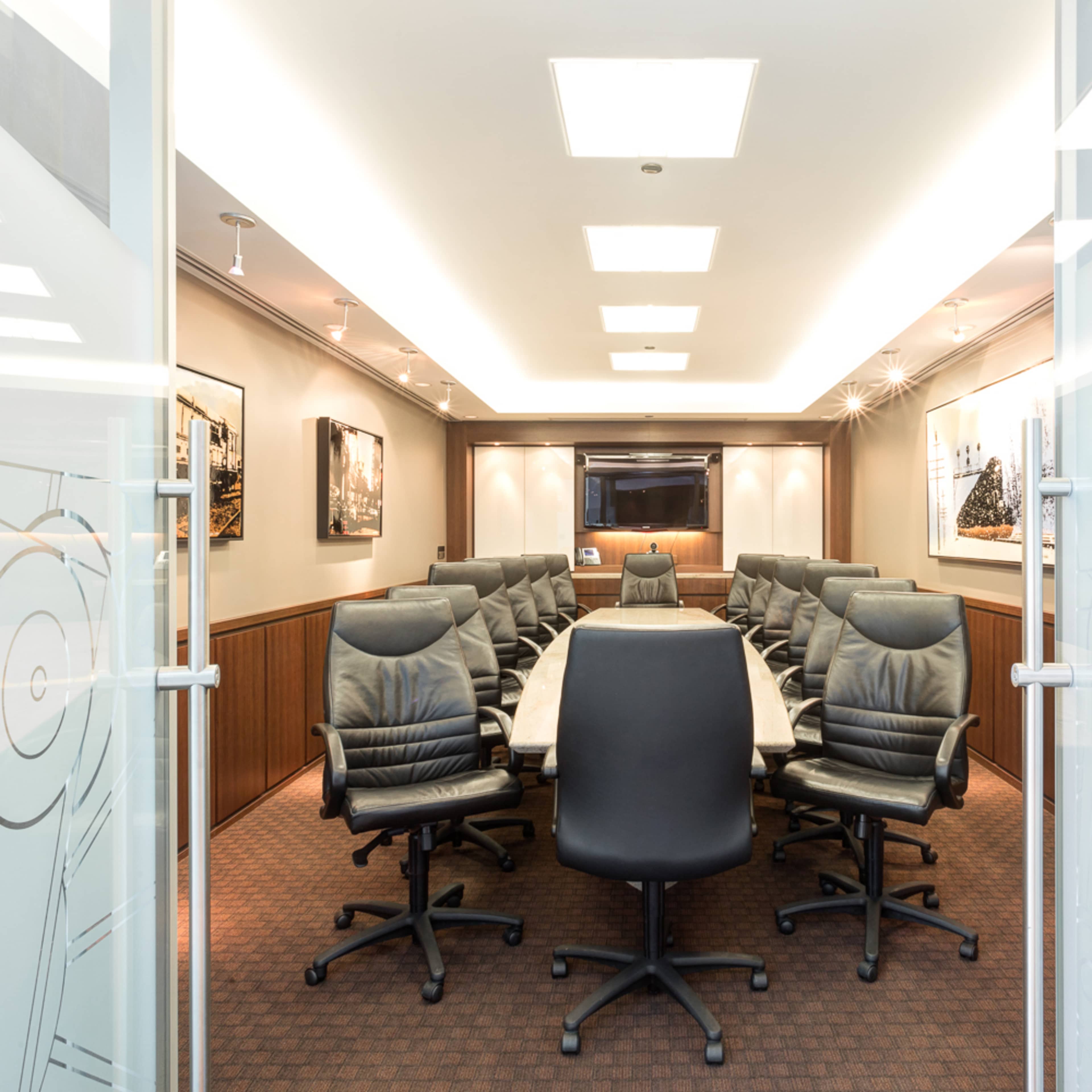 A large conference room with a rectangular table surrounded by high-backed chairs, featuring a television and artwork on the walls.