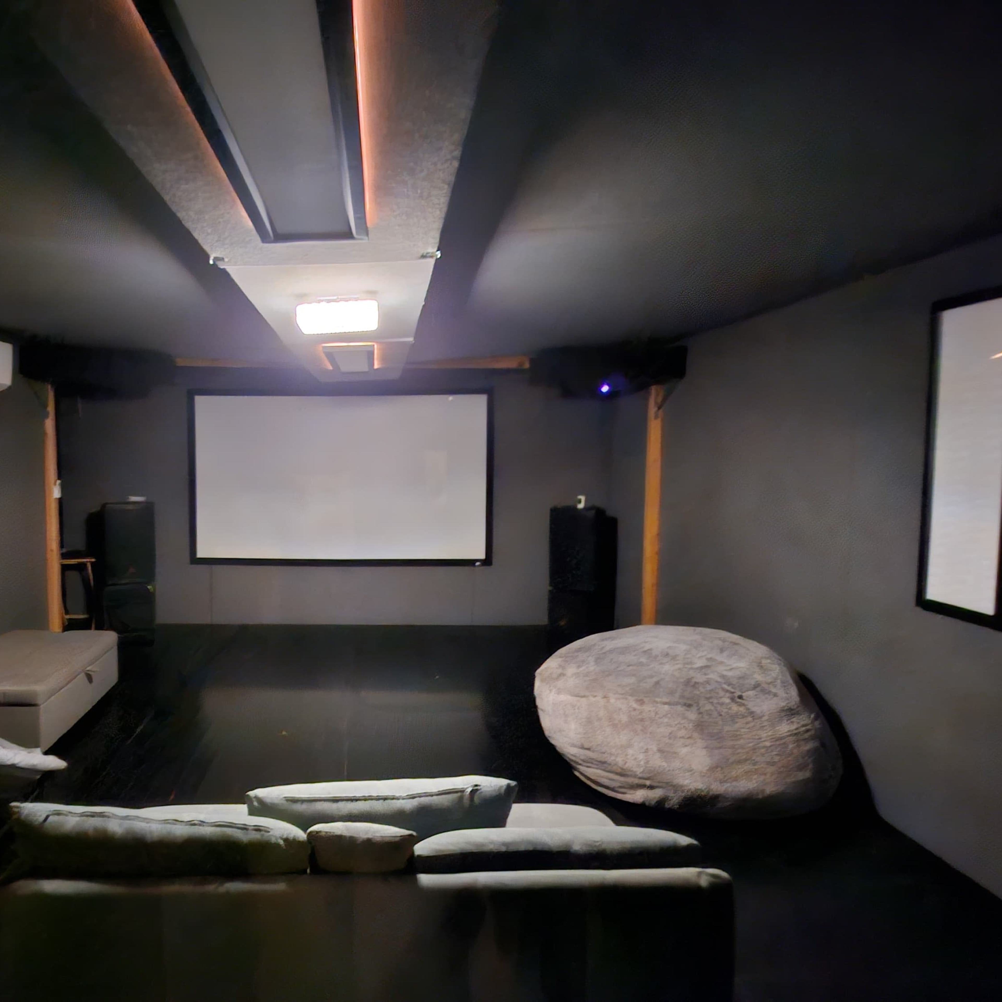 A dark, enclosed home theater room with a large screen at the front, seating arrangements, and sound equipment.