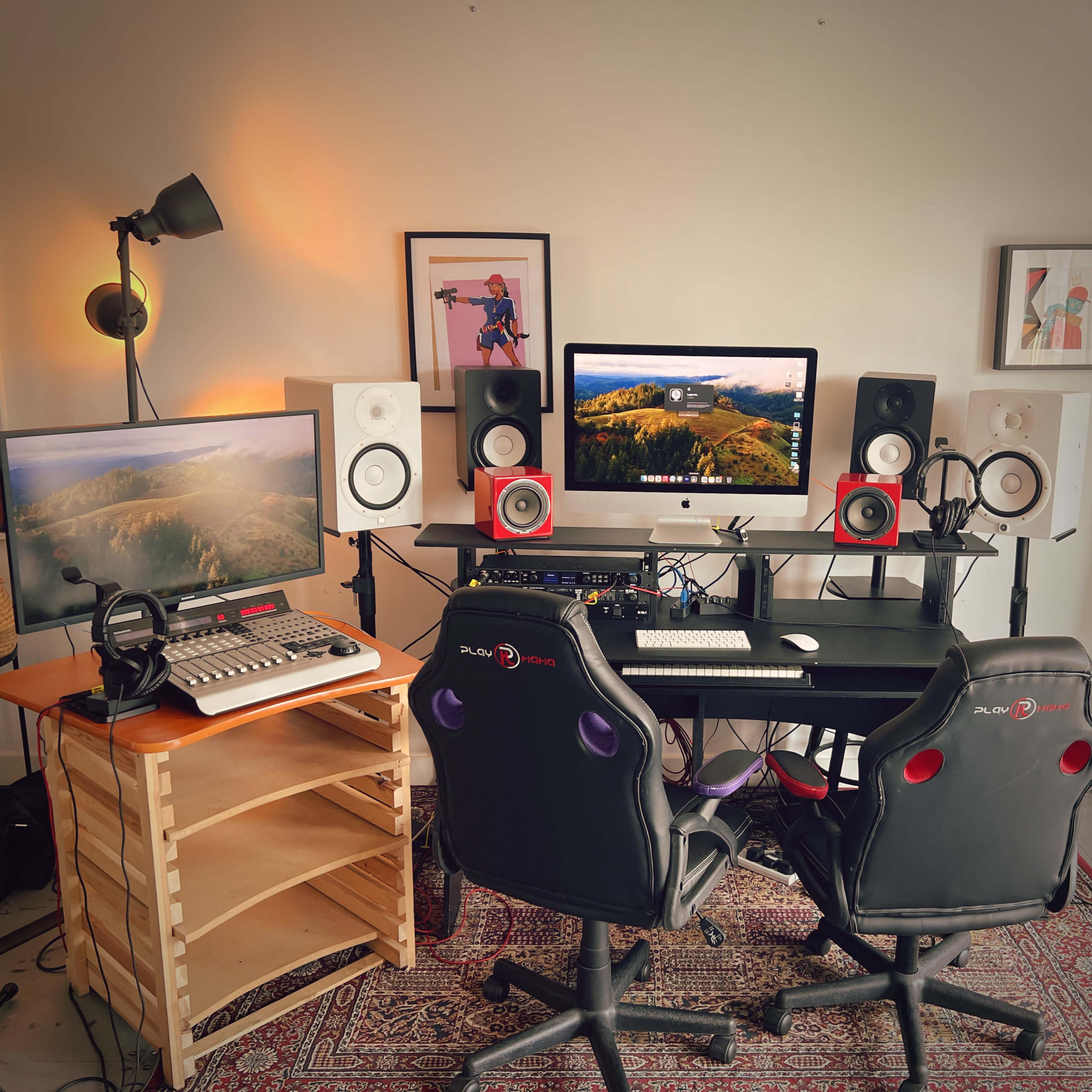 A music production workspace with two black chairs facing a desk equipped with monitors, speakers, and audio equipment.