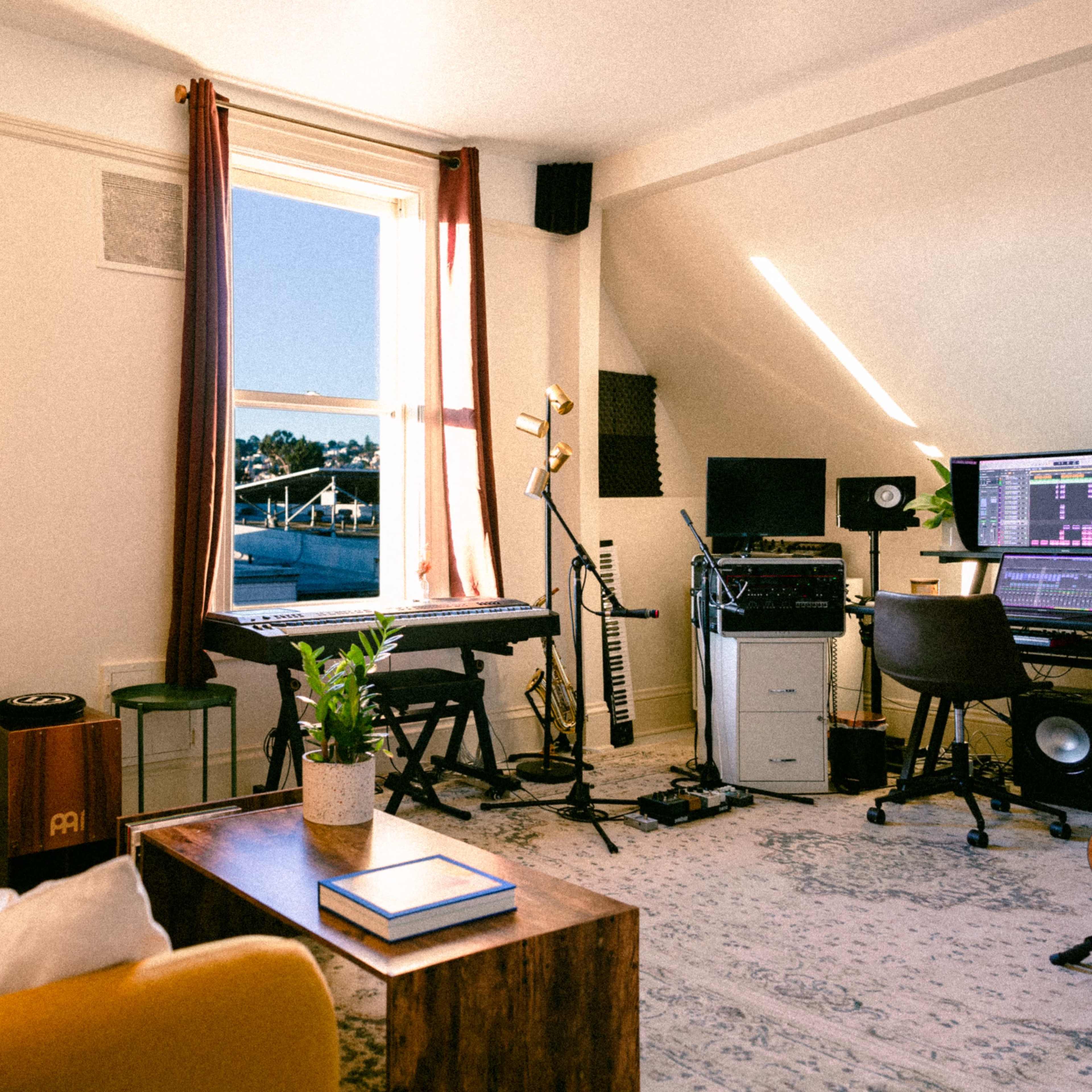 The scene shows a cozy room featuring a yellow sofa, a wooden coffee table, a keyboard and microphone set up, and a computer workstation with music equipment, illuminated by natural light coming through a window.