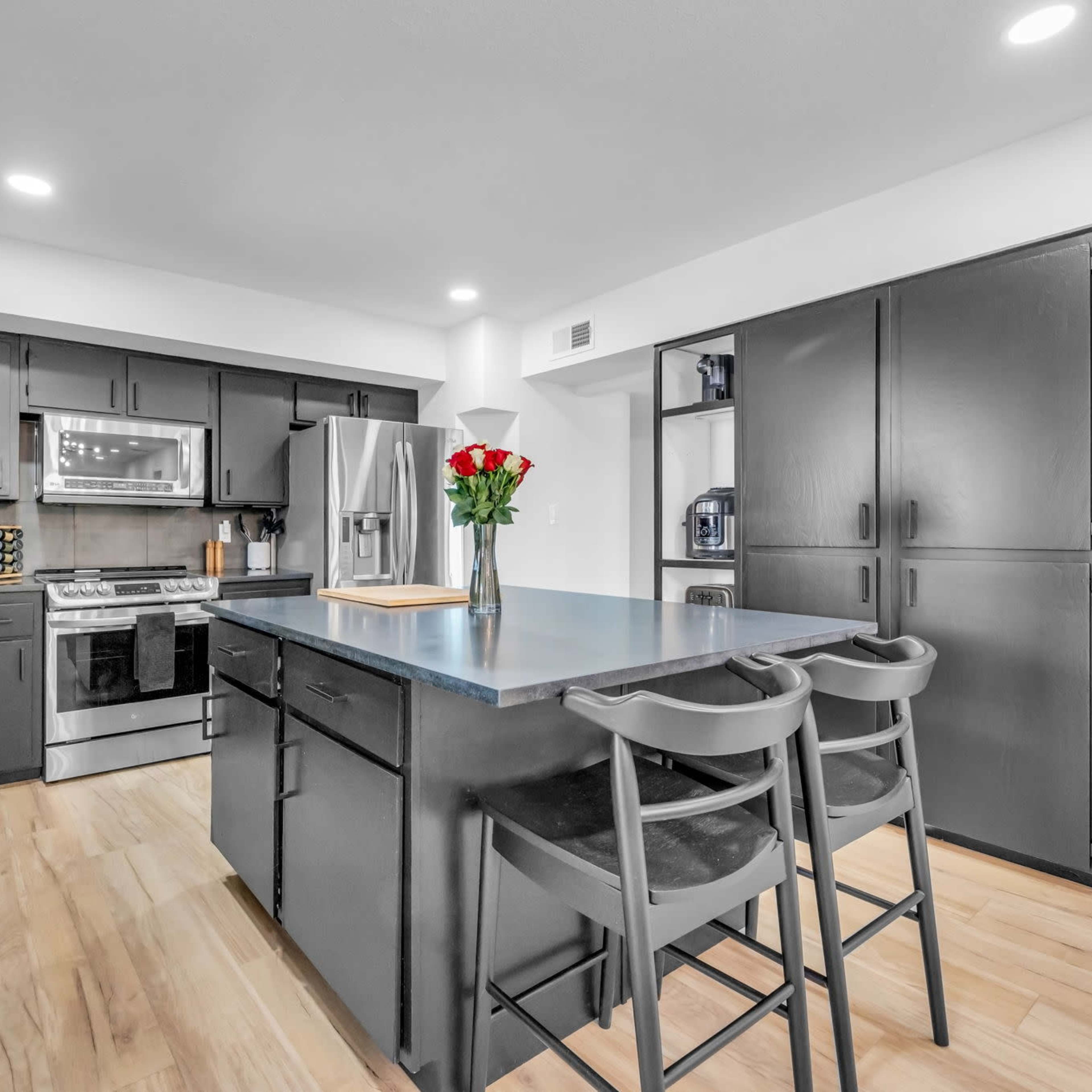 A modern kitchen features black cabinetry, stainless steel appliances, and a central island with bar stools.