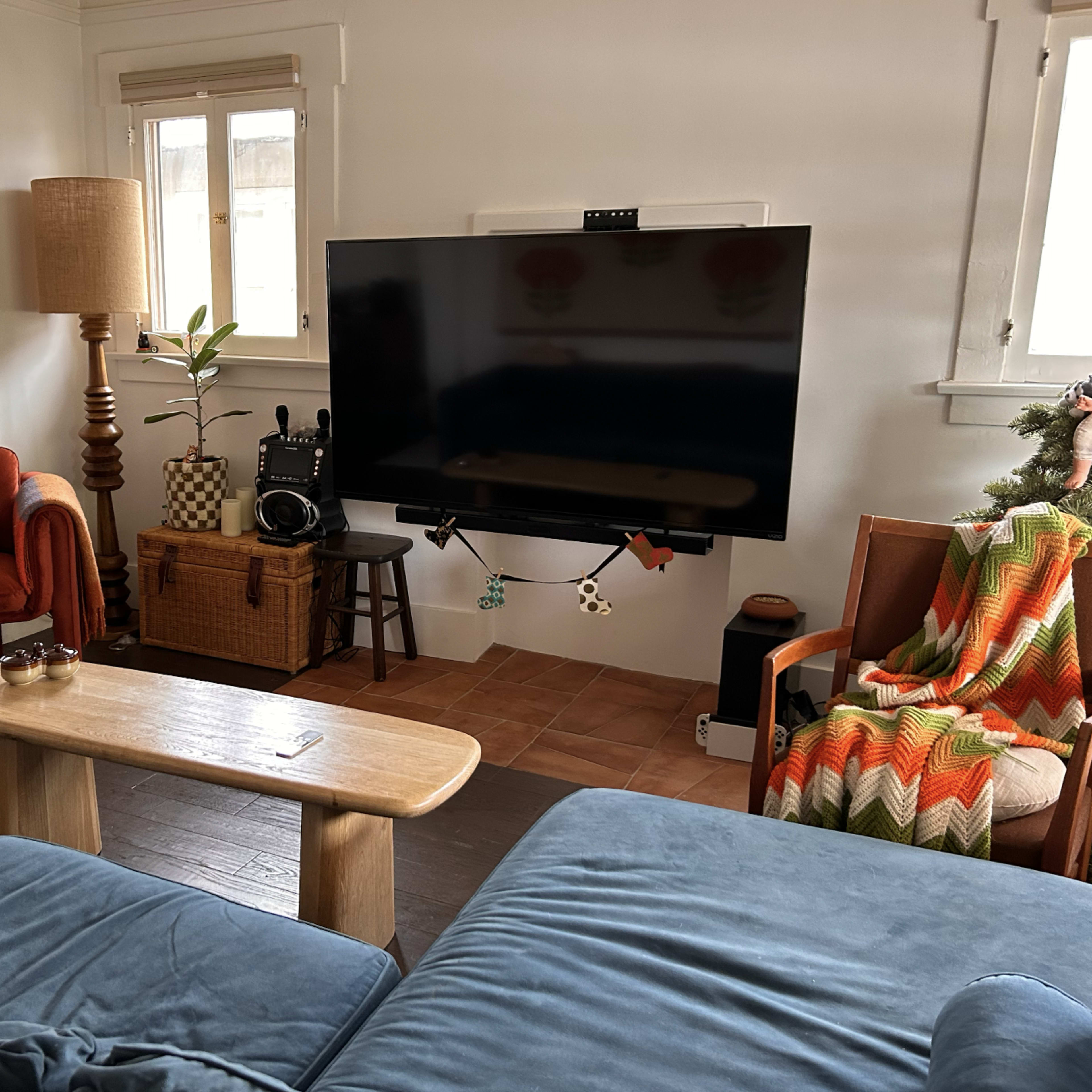 A cozy living room with blue couches, a wooden coffee table, a mounted television, and decorative elements including a lamp and a colorful blanket.