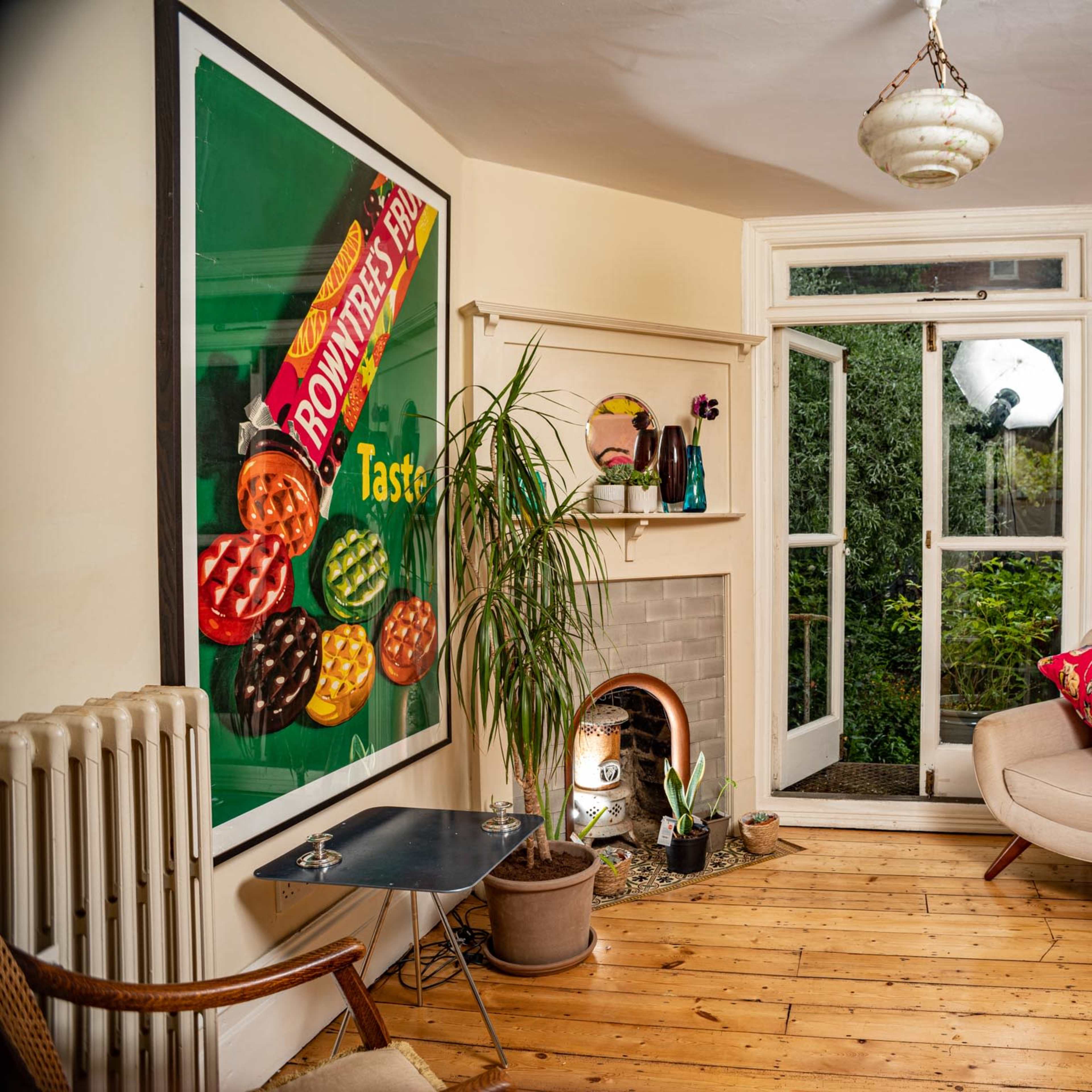 A cozy living room featuring colorful artwork on the walls, a small fireplace, and a door opening to a garden.