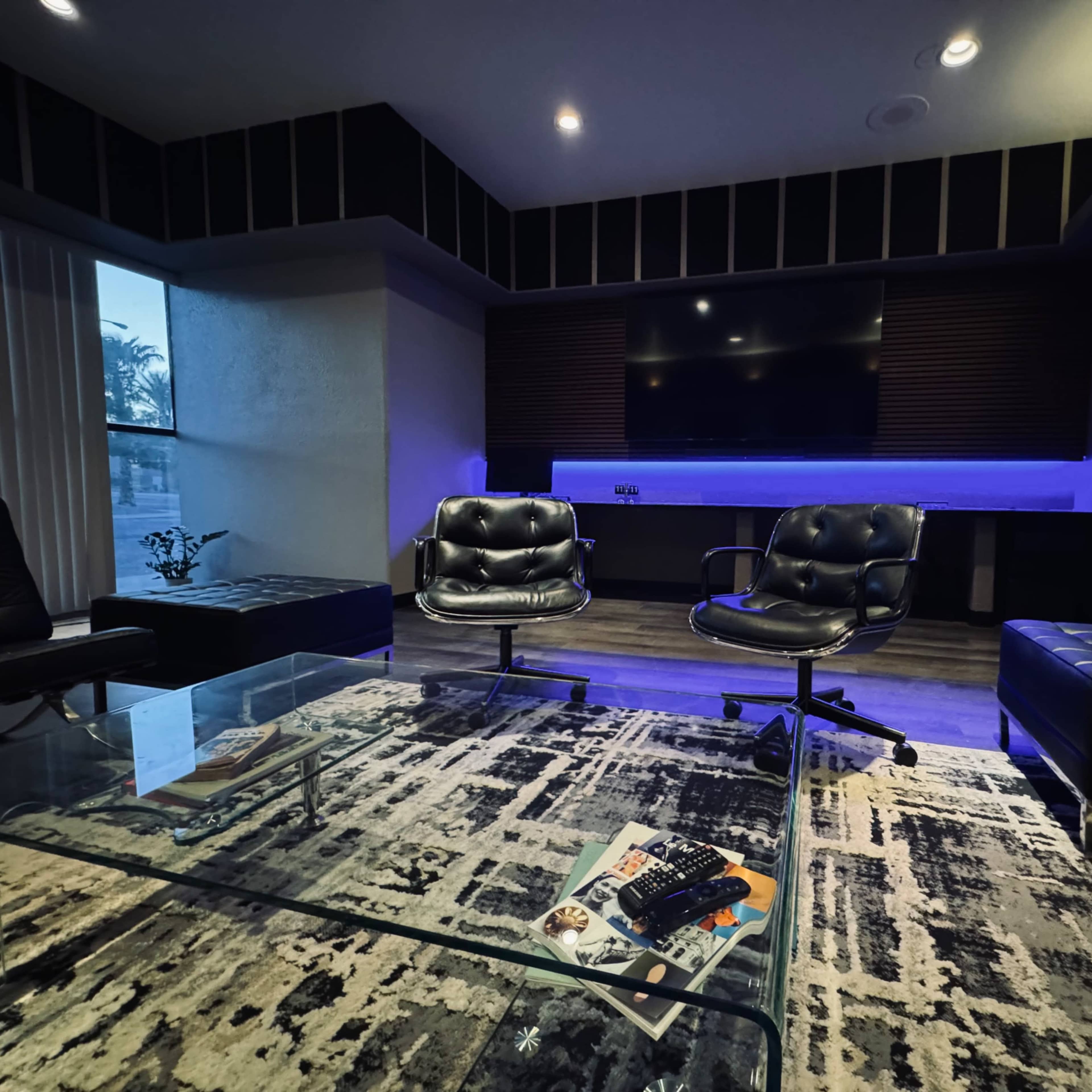 A modern lounge area with black leather seating, a large screen displaying a city skyline, and a rug on a dark floor.