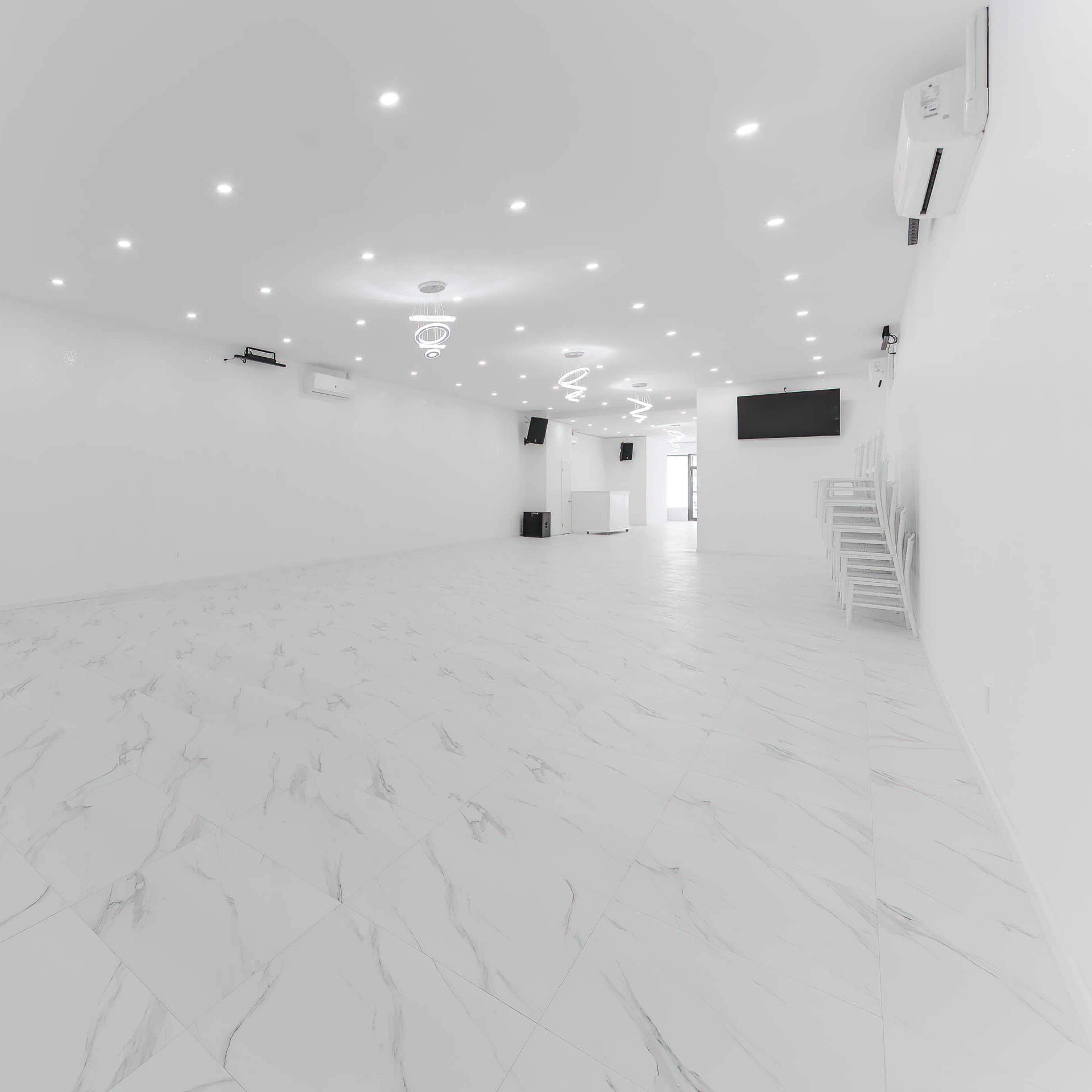 A spacious, empty room with white walls, a tiled floor, and modern lighting fixtures.